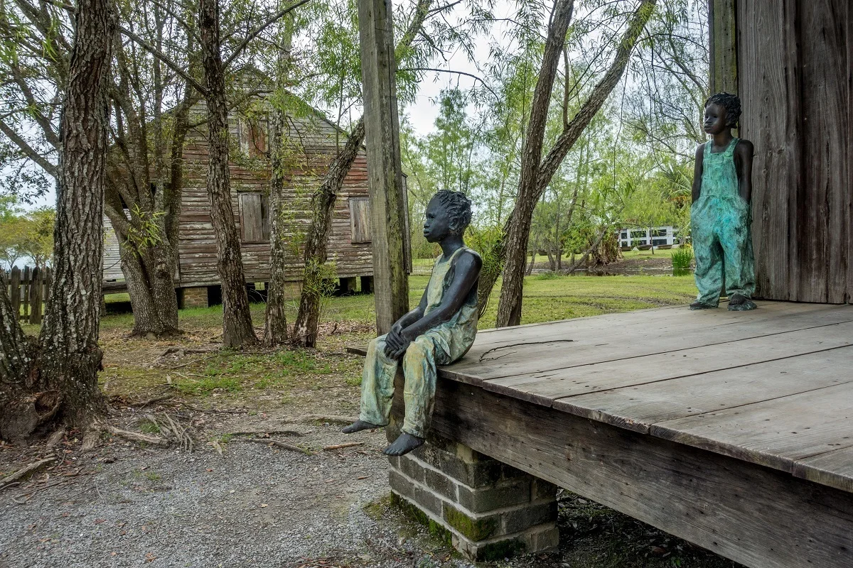 Statues representing enslaved children on the porch of former slave quarters.