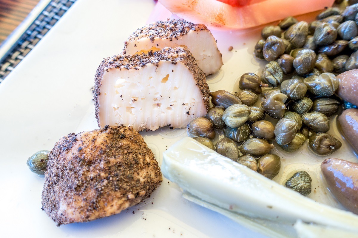 Maltese cheese coated in pepper beside capers on a plate