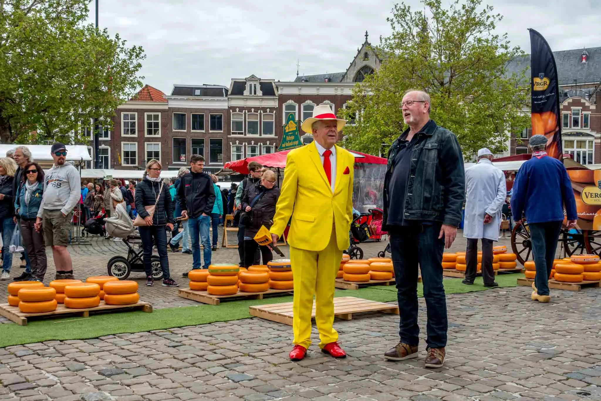 Man in yellow suit with a microphone beside rows of cheese