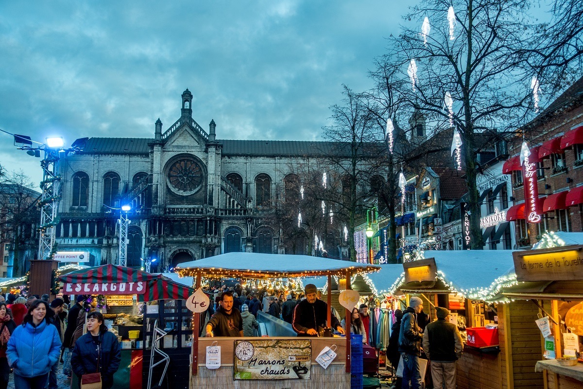 Shoppers at Christmas market stalls with church in the background.