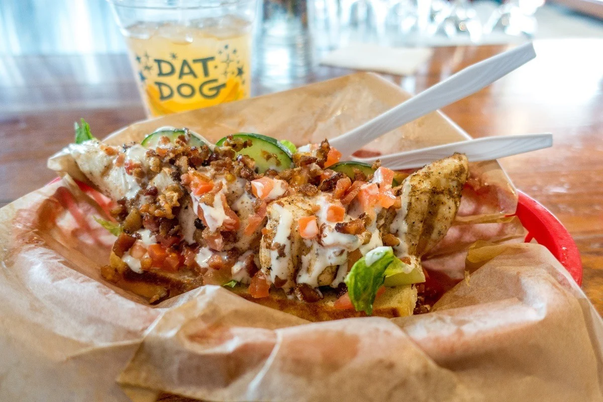 Hot dog bun piled with toppings on a table with an orange drink.