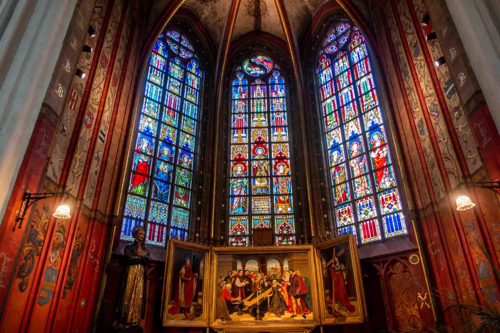 Three panels of stained glass behind a triptych painting inside the Antwerp cathedral 