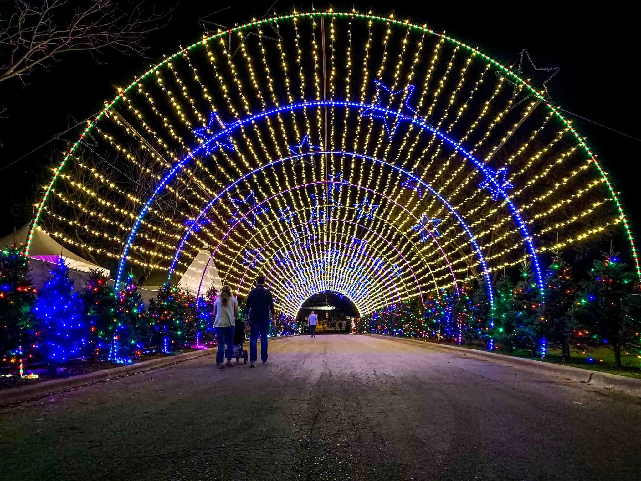 People walking through a tunnel of Christmas lights at night