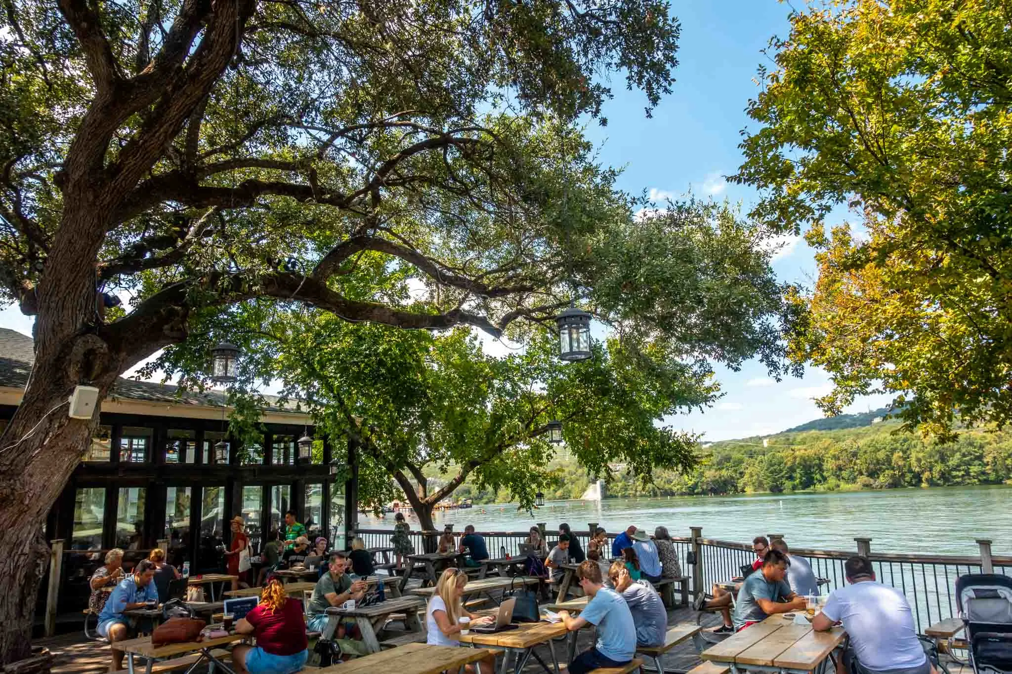 People sitting at picnic tables on a patio by a lake