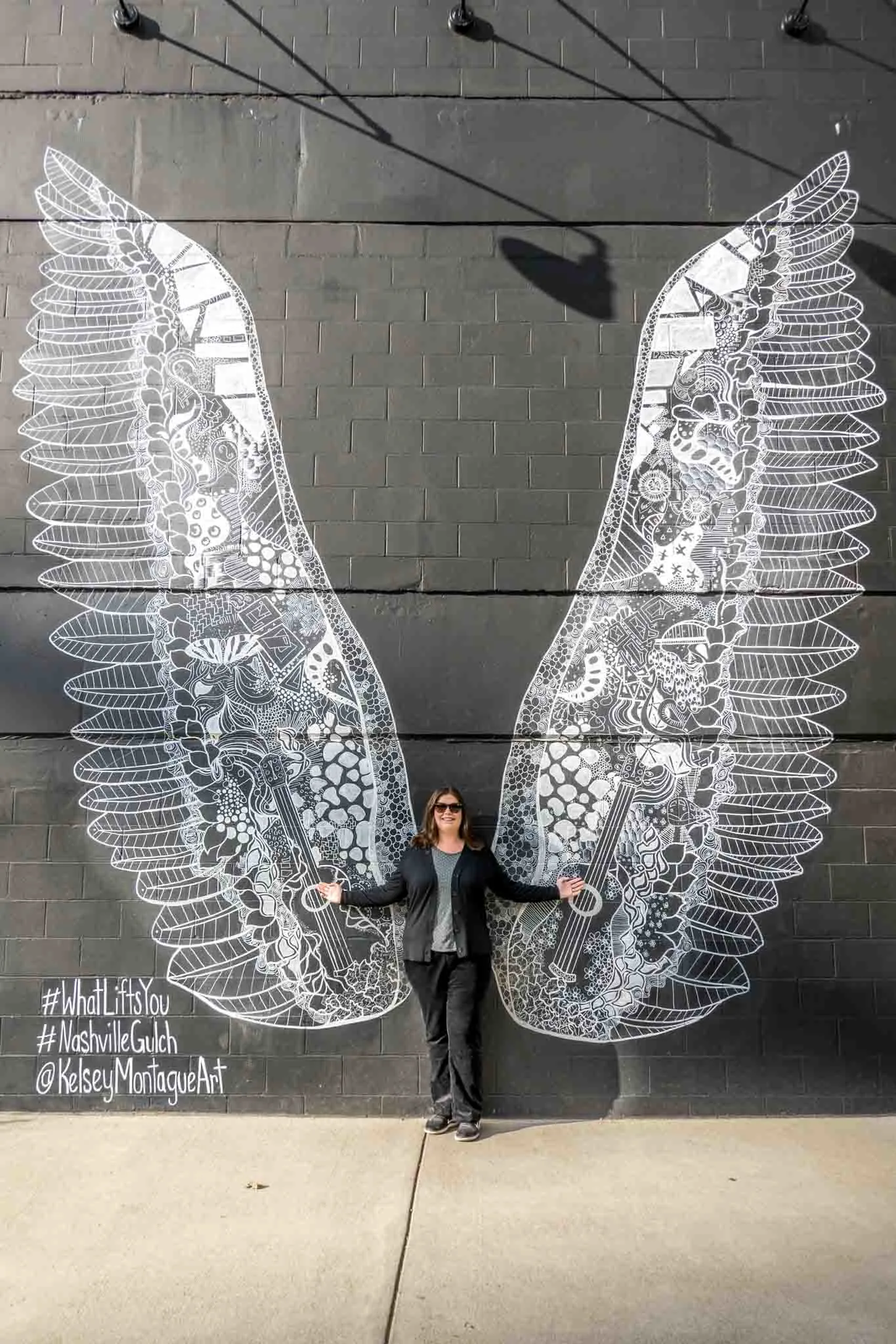 Person posing with mural of large white wings