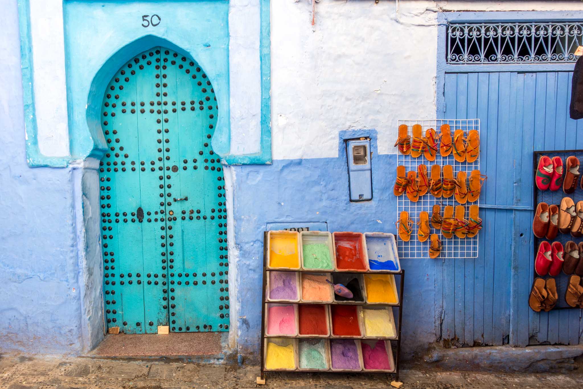Multi-colored pigments and sandals for sale next to a turquoise door