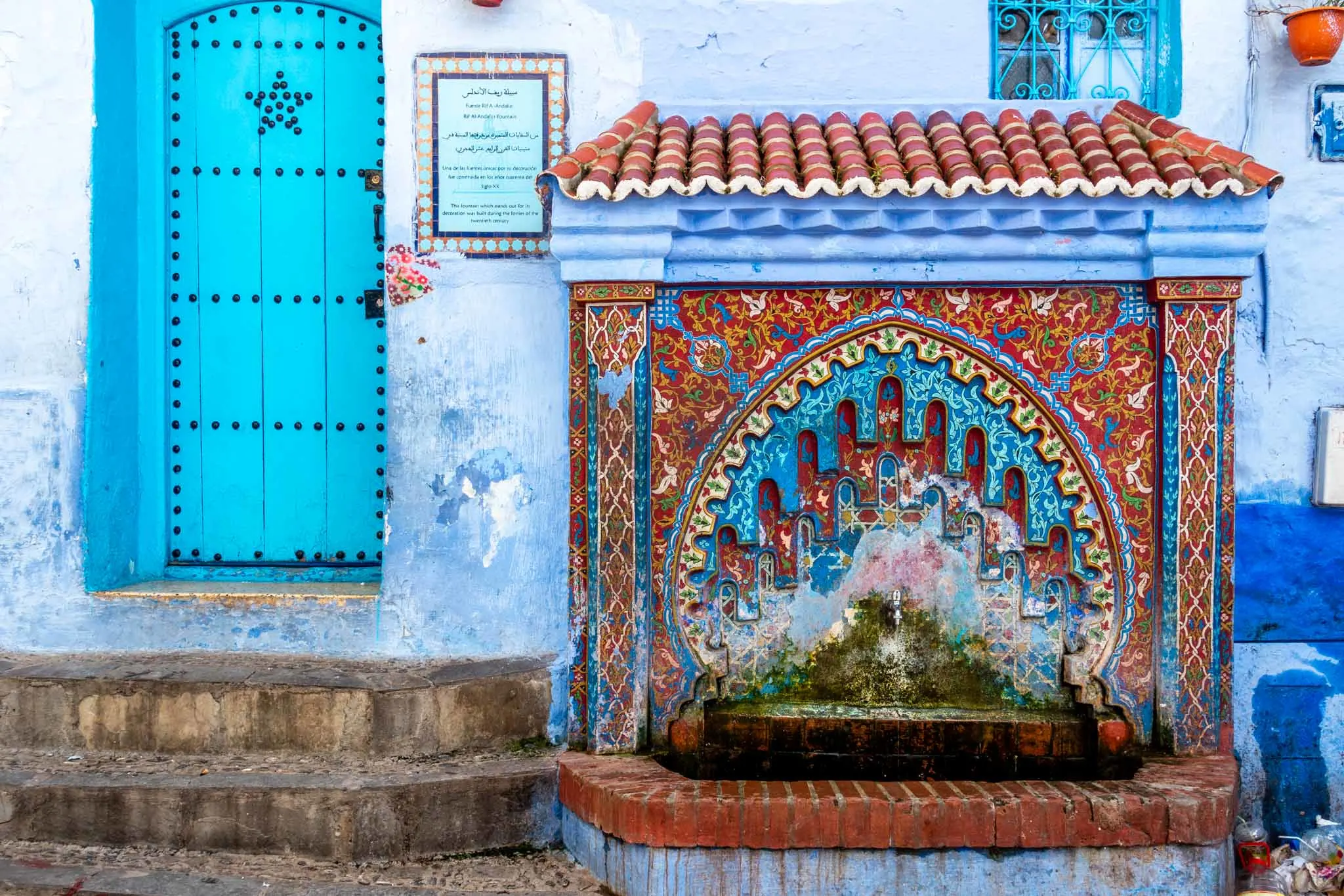 Red and blue decorated fountain next to a turquoise door
