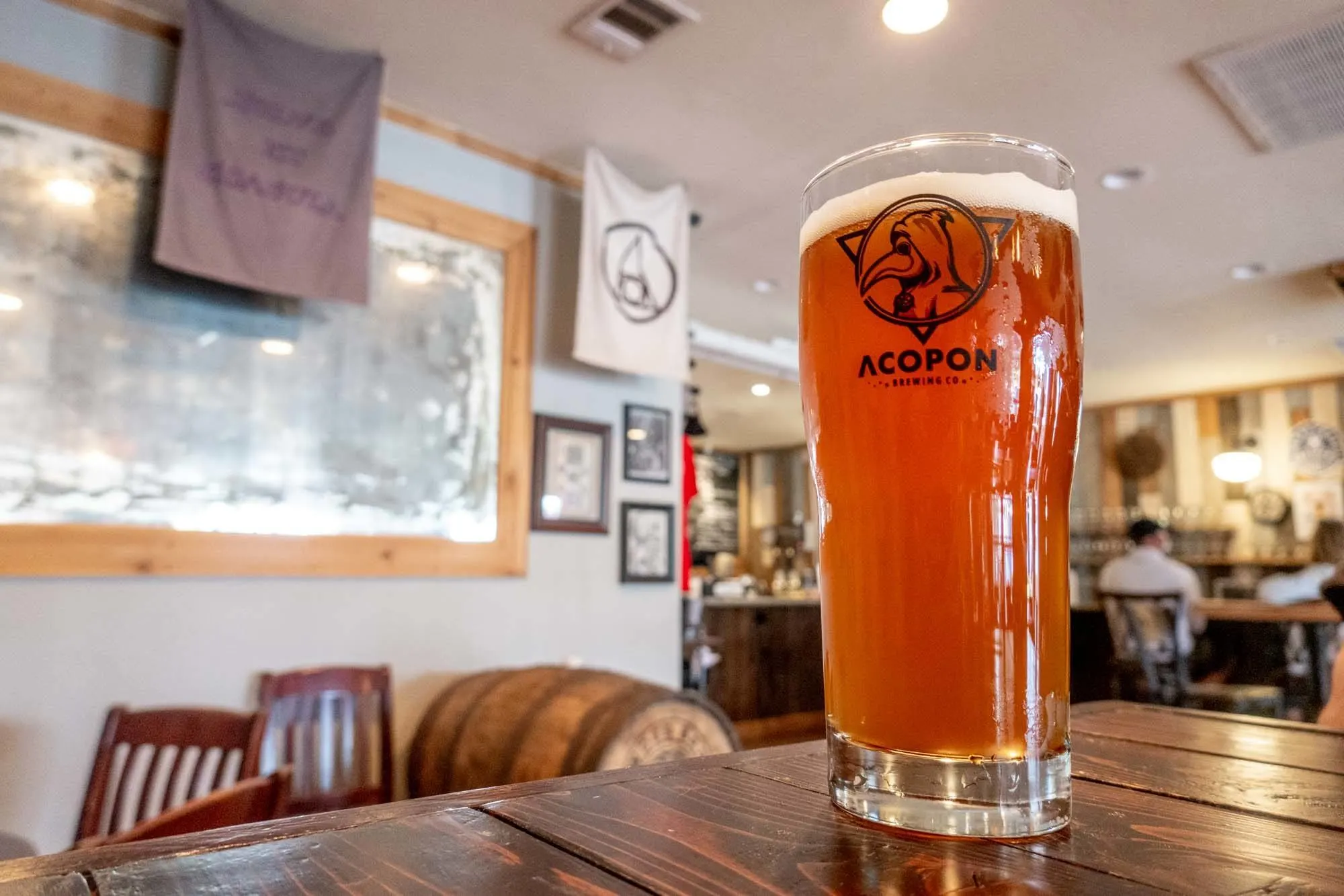 Pint glass with Acopon Brewing Co. logo on a table in a bar.