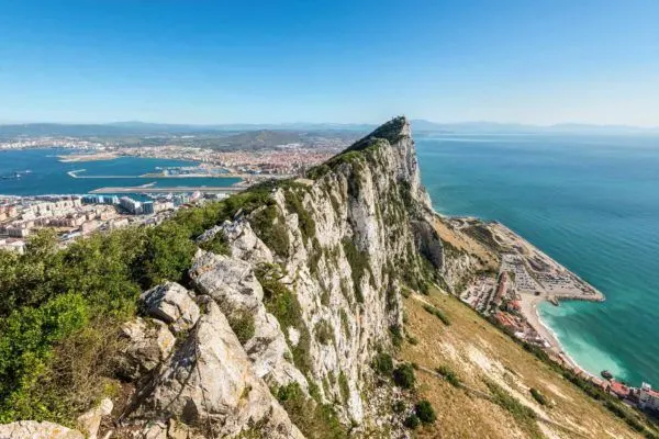 Massive rock peak above the ocean with a city below