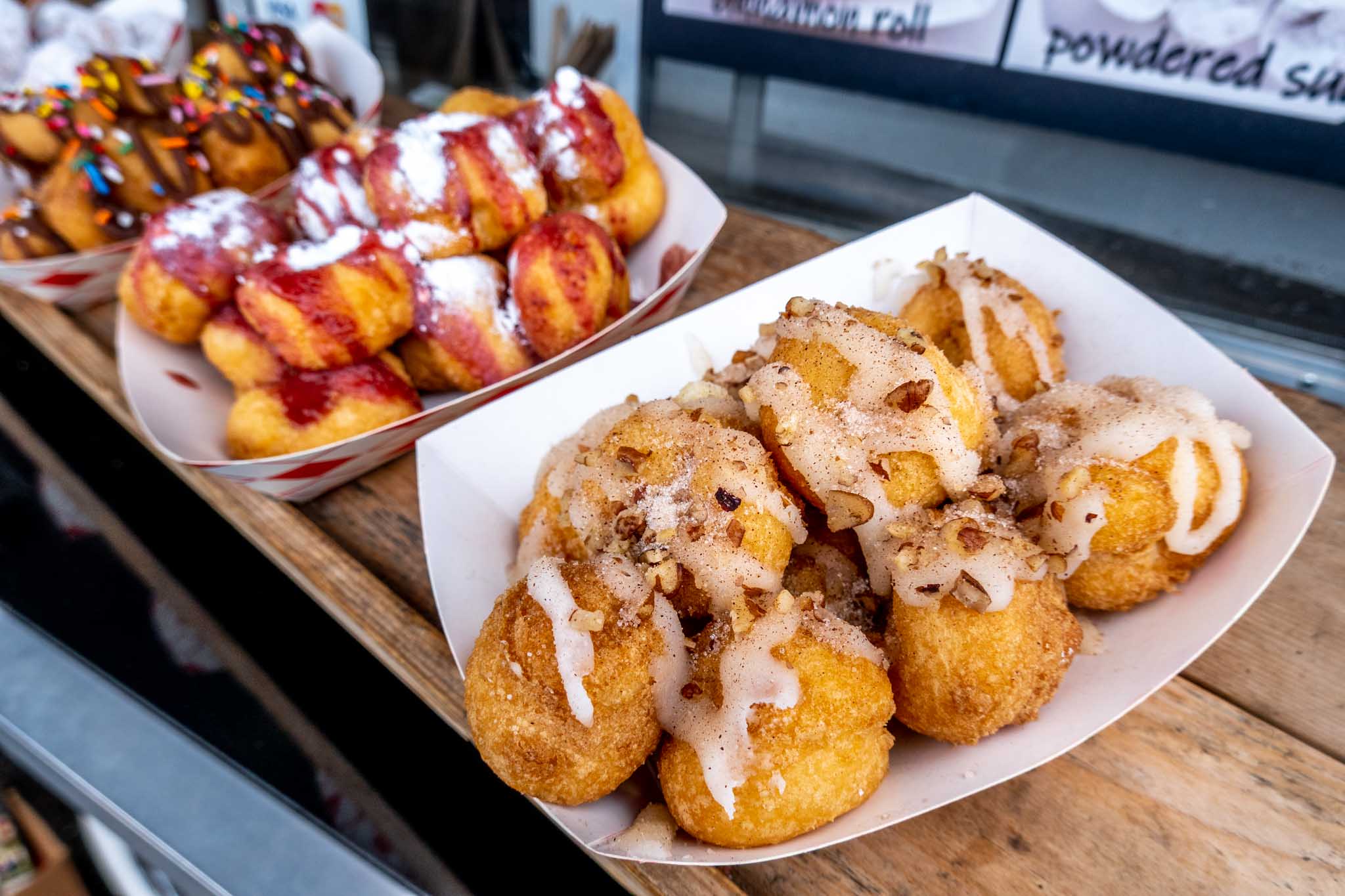 Piles of small donuts topped with chocolate, strawberry, and icing.