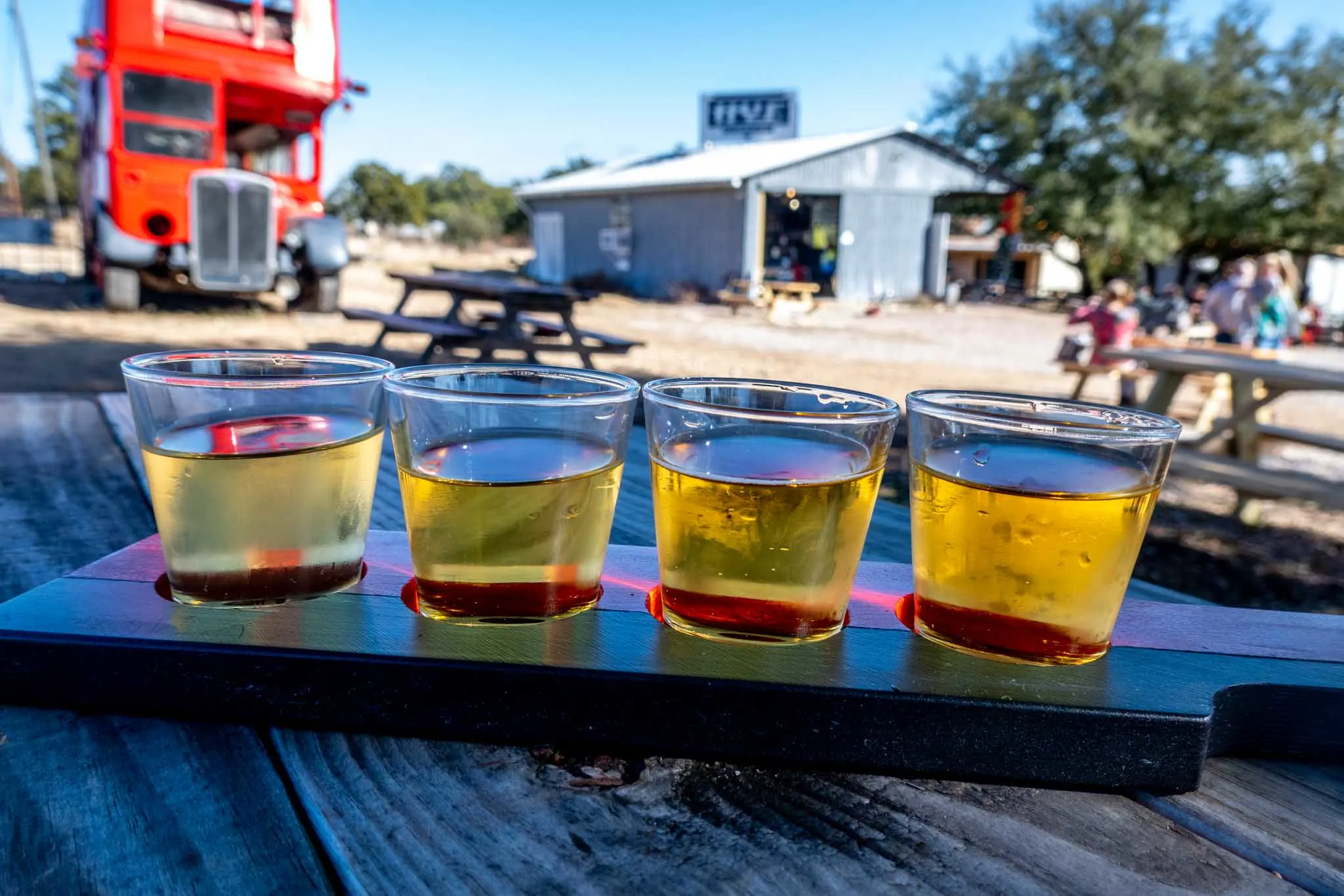 Flight of 4 glasses of cider on a picnic table 