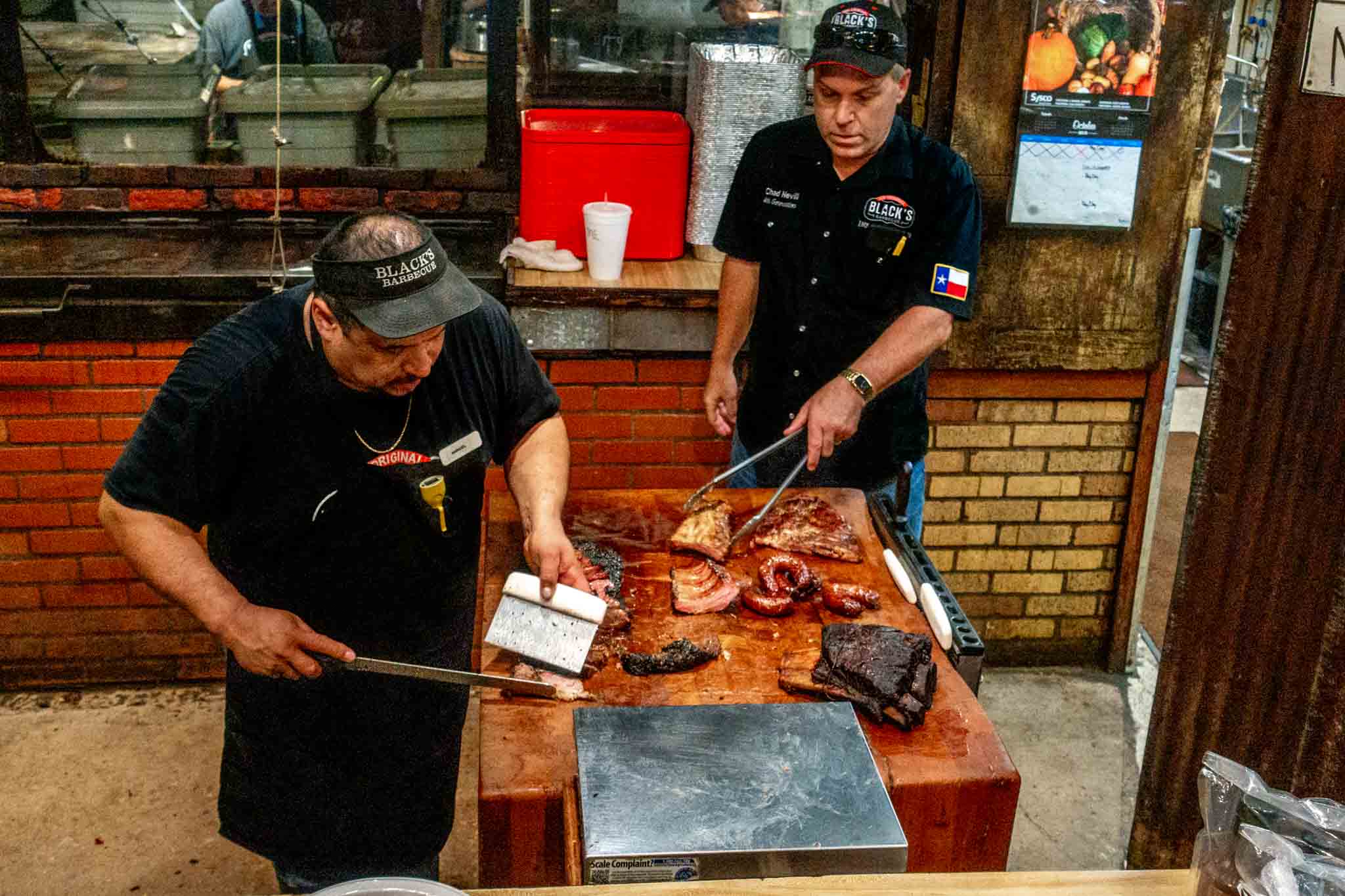 Two men carving and serving barbecue on a wood black in a restaurant kitchen