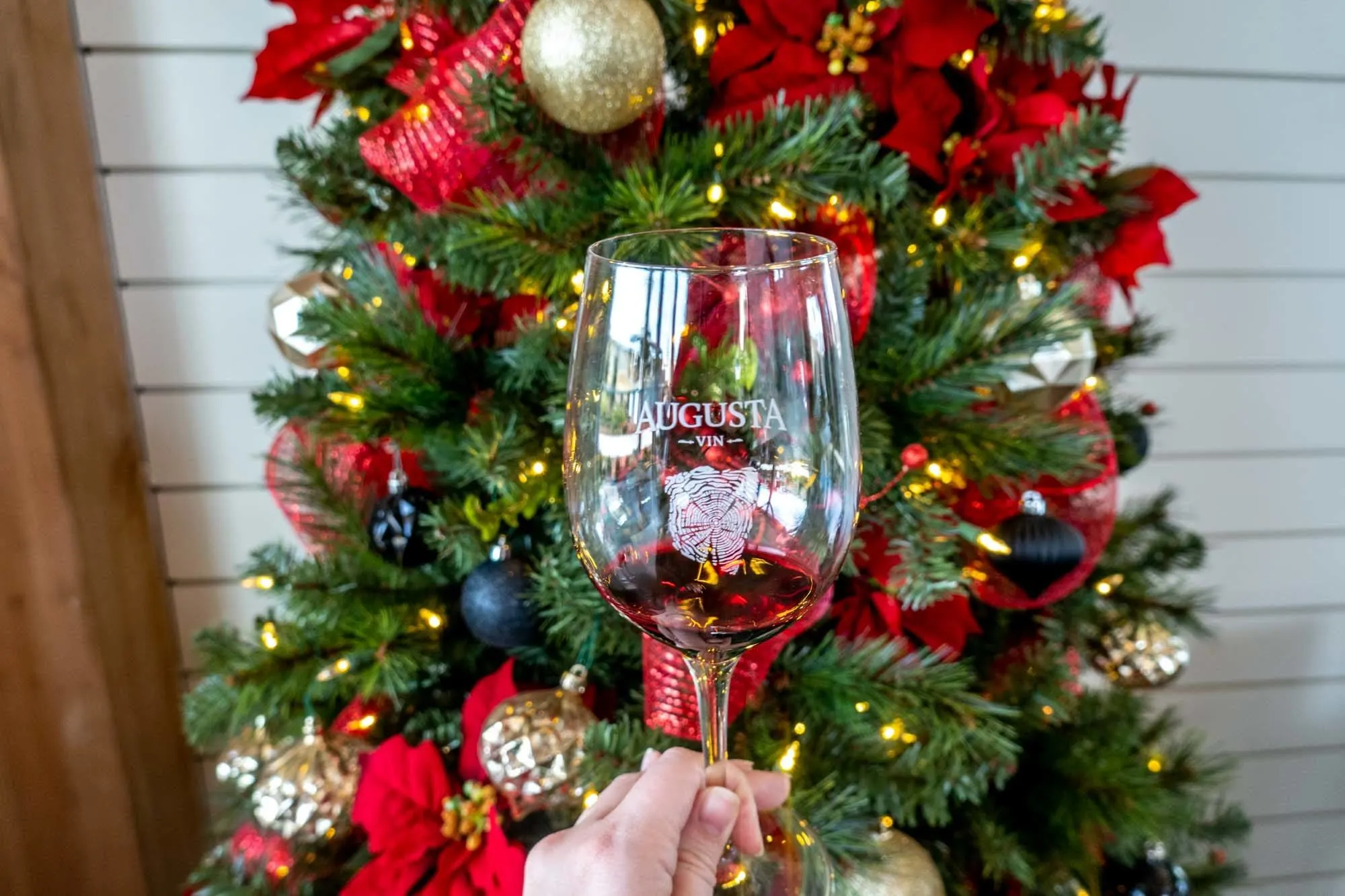 A wine glass labeled "Augusta Vin" in front of a Christmas wreath