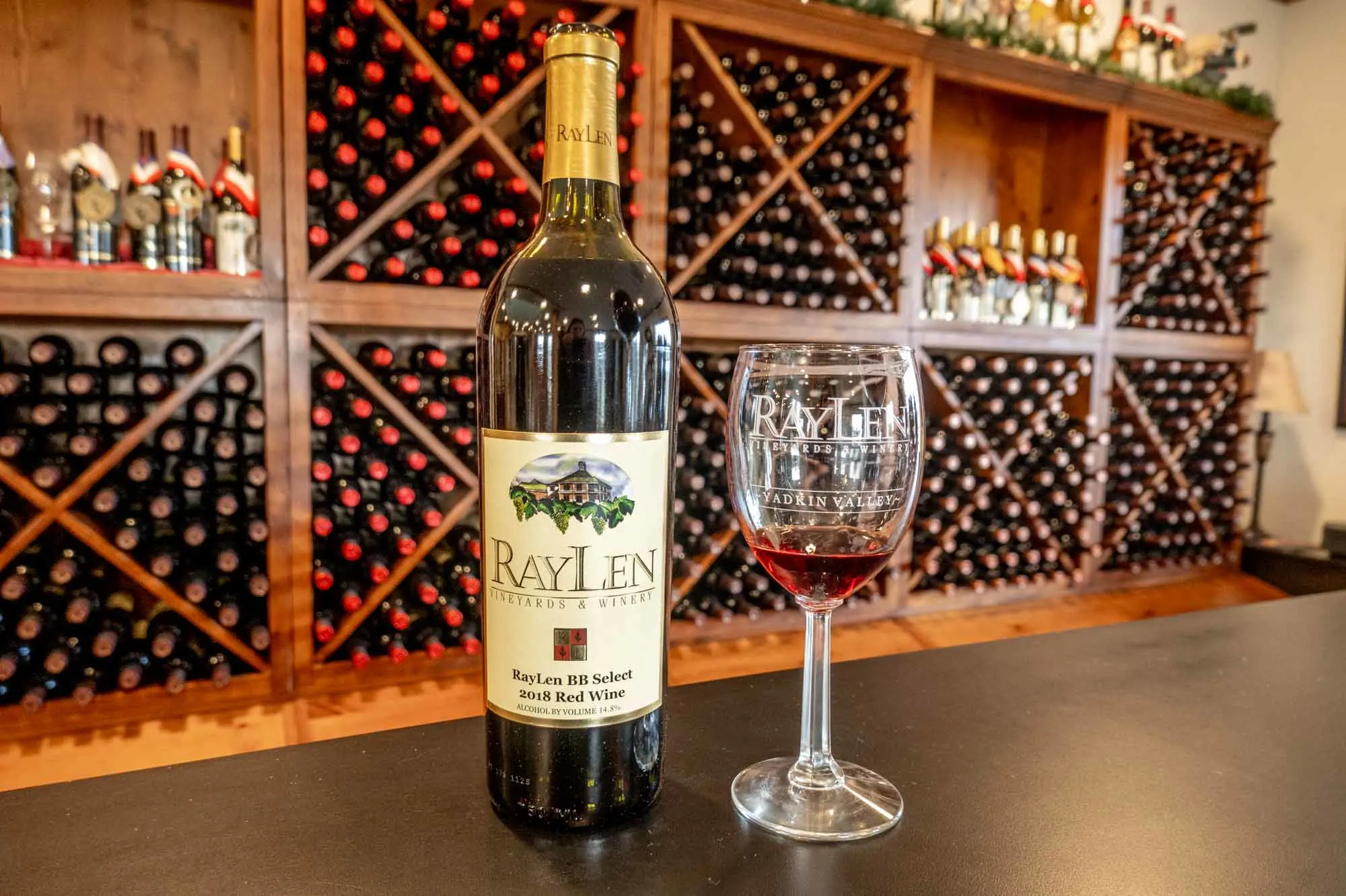 Bottle of red wine labled for RayLen Vineyards on a counter beside a glass of red wine