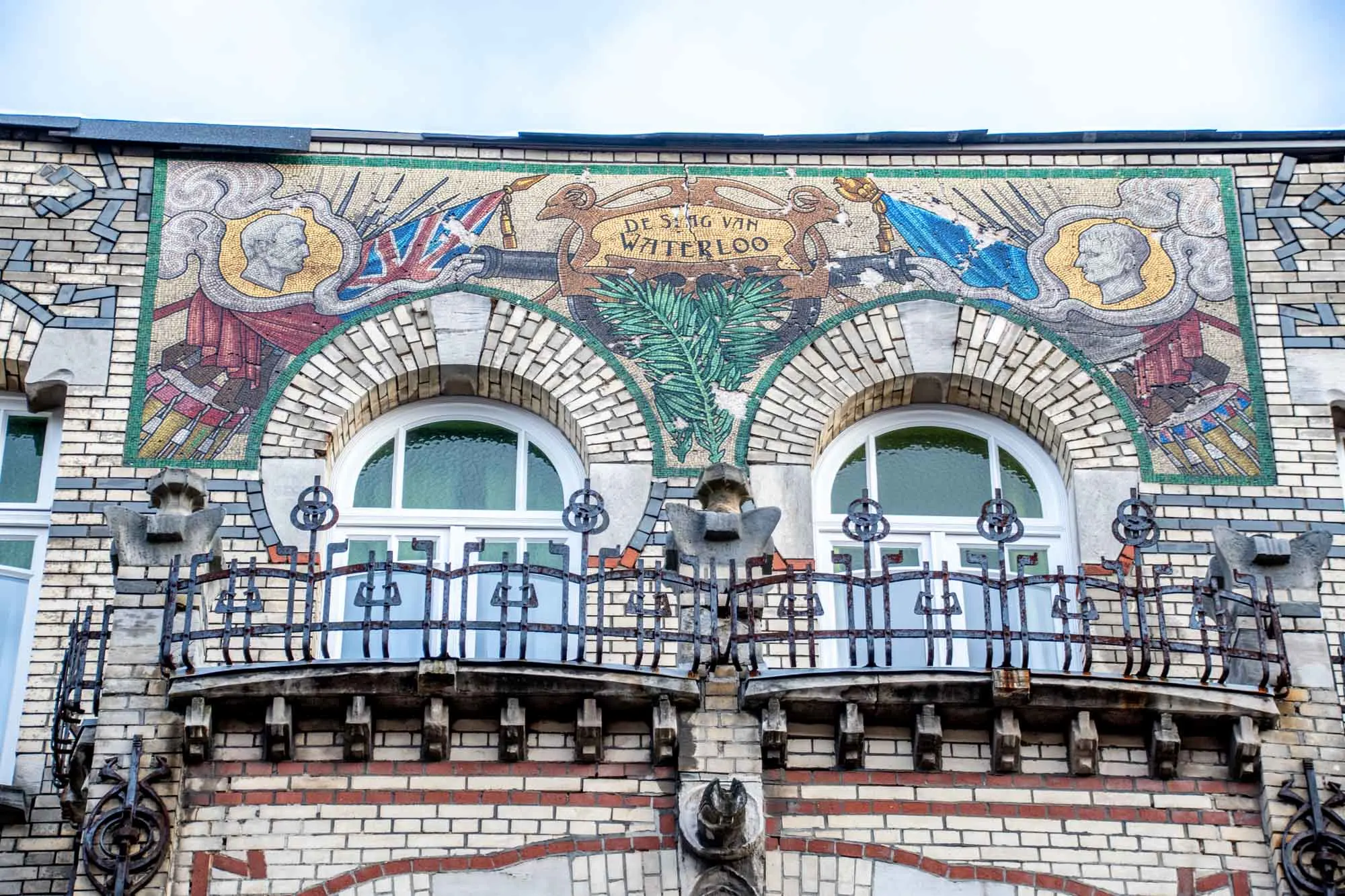 Exterior of a building with a colorful mosaic, rounded windows, and intricate iron balconies