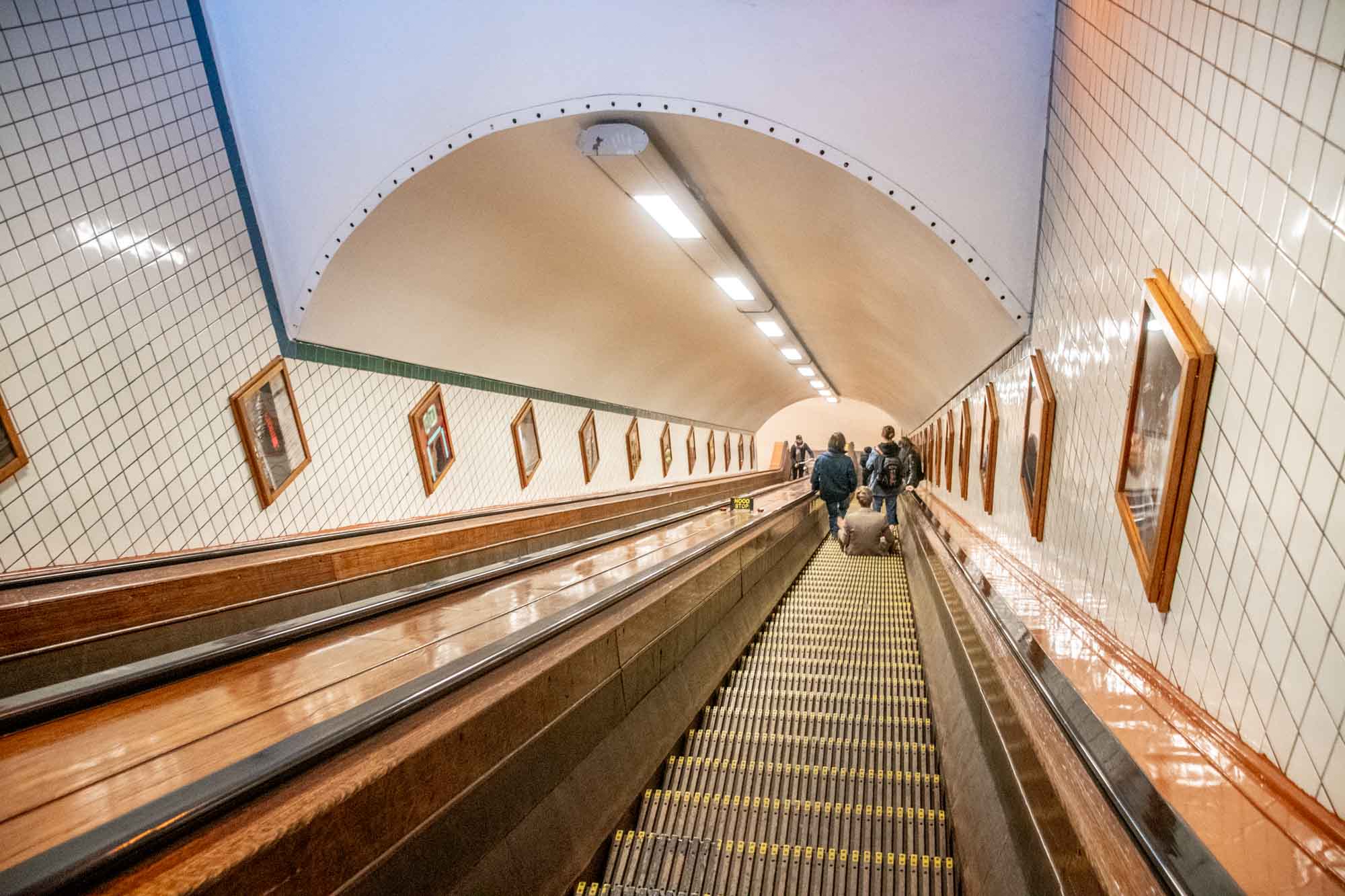 Wooden escalator descending deep into a tunnel with white tile on the walls