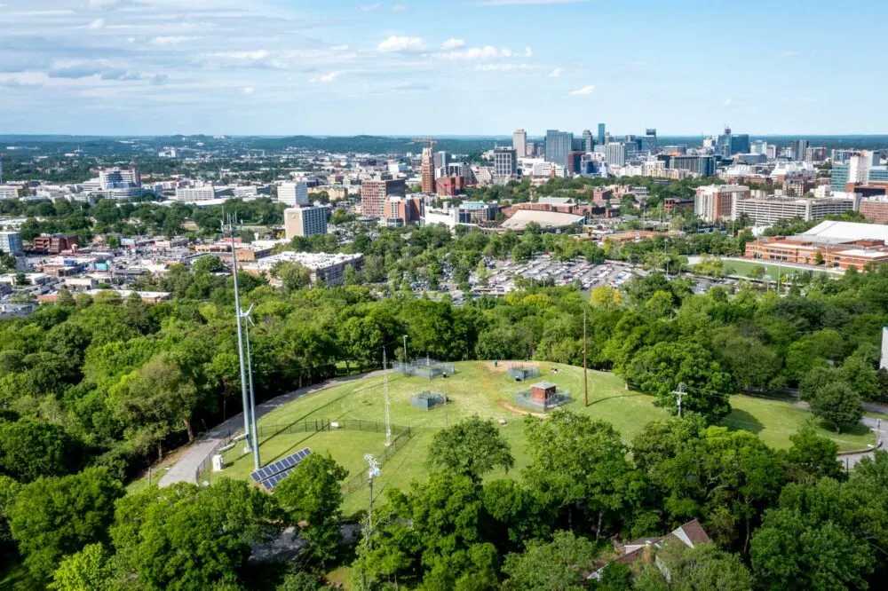 Overhead view of a park surrounded by trees that has a view of buildings in downtown