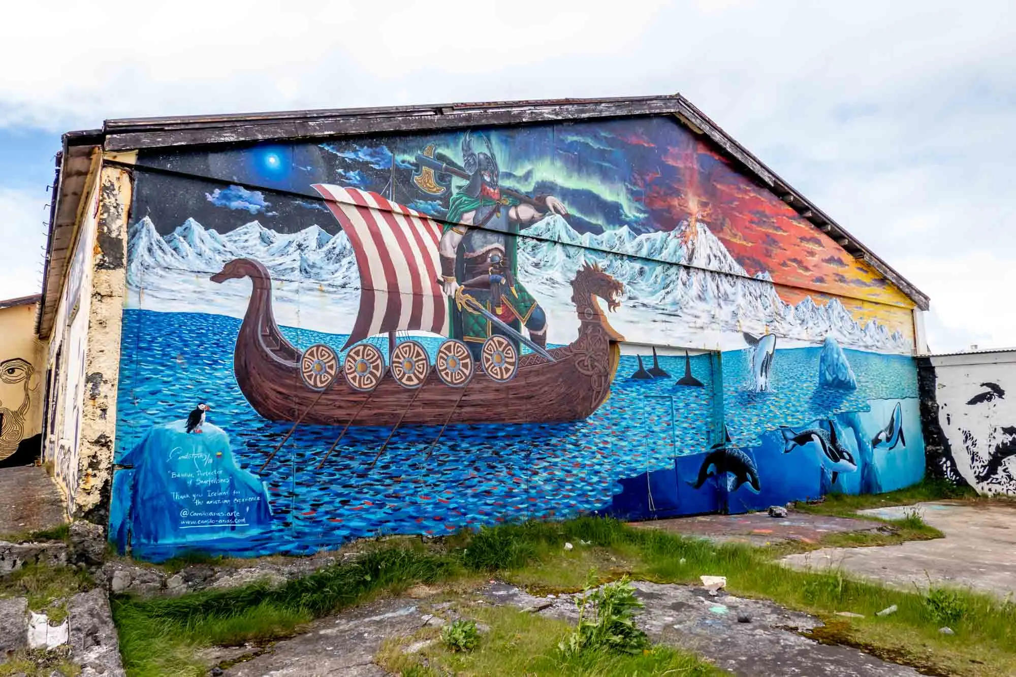 Street art mural of Bardur sailing on Viking ship in front of exploding volcano with puffins and orcas in the water