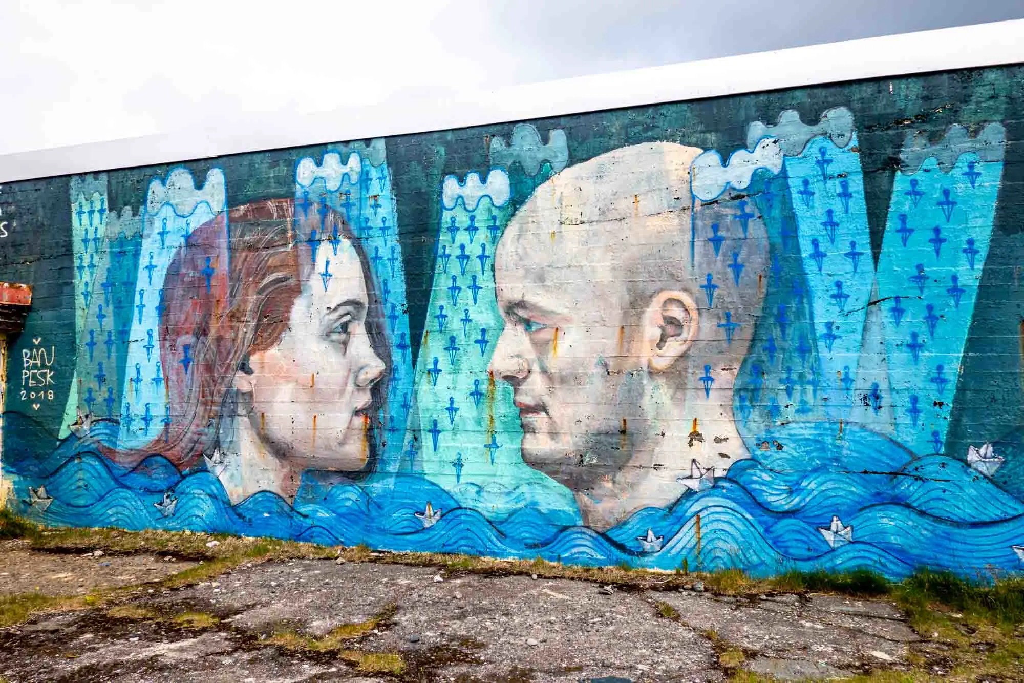 Blue wall mural of man and woman's heads facing each other above the ocean waves