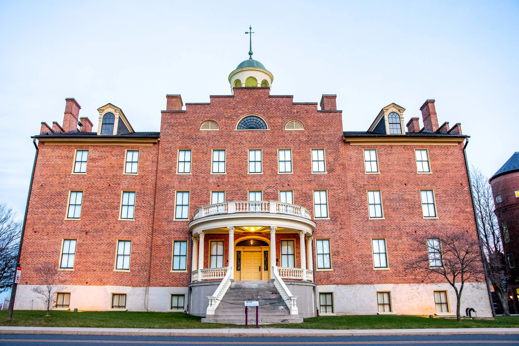 Large red brick building with a front porch, staircase, and cupola on top.