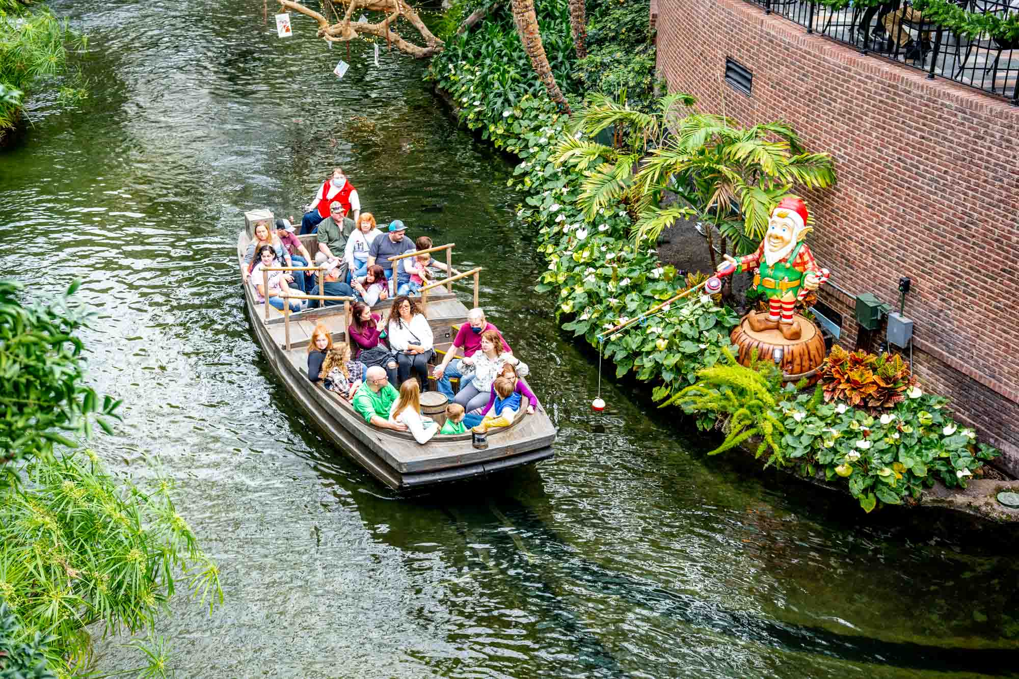 People in a boat cruising on an indoor river at they pass a brick wall.