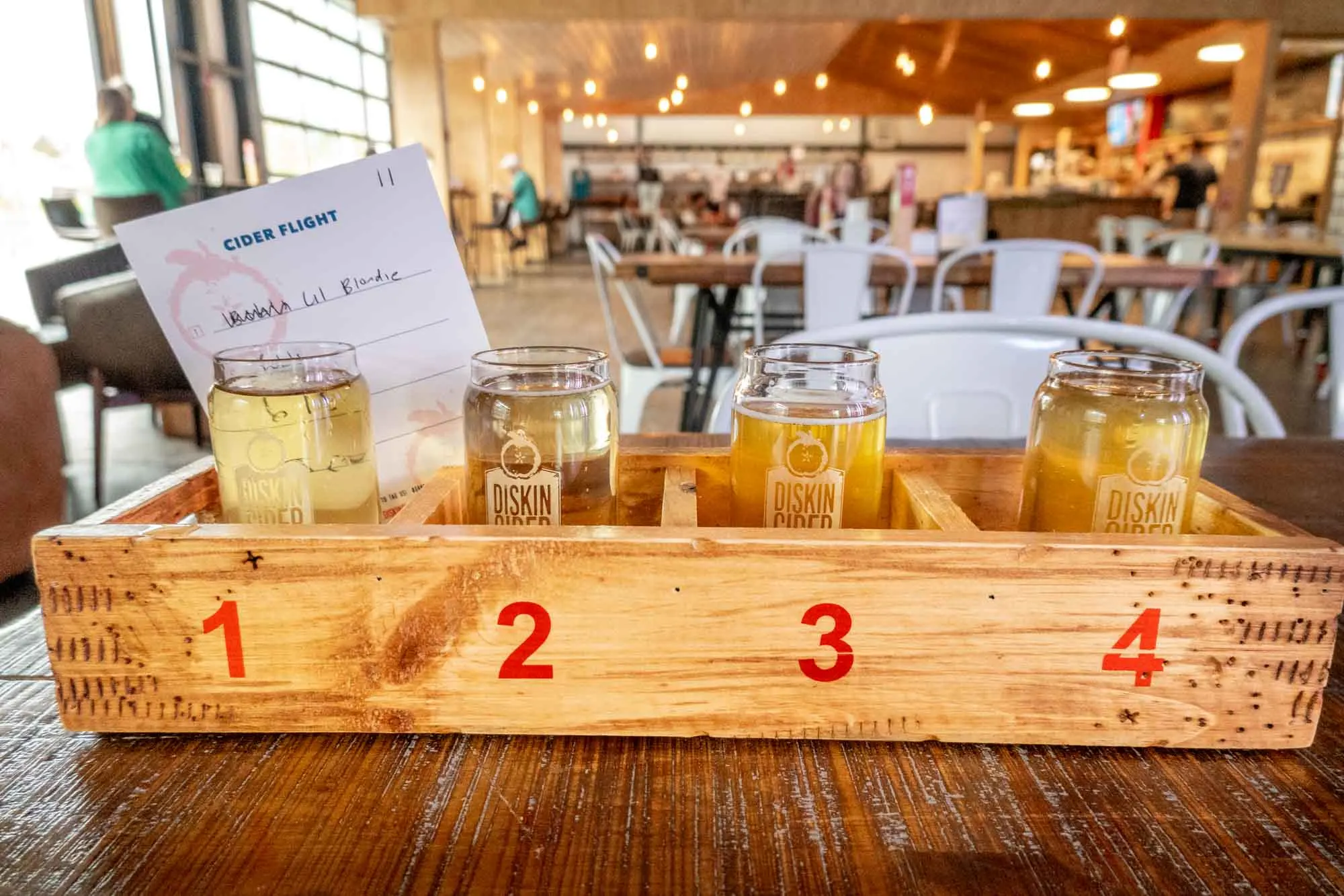 Flight of 4 glasses of hard cider in a wooden carrier on a table.
