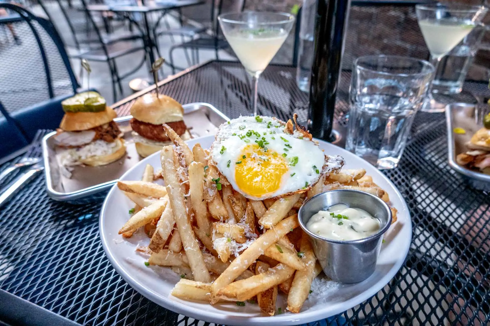 Sliders on a platter next to a plate of French fries topped with a fried egg