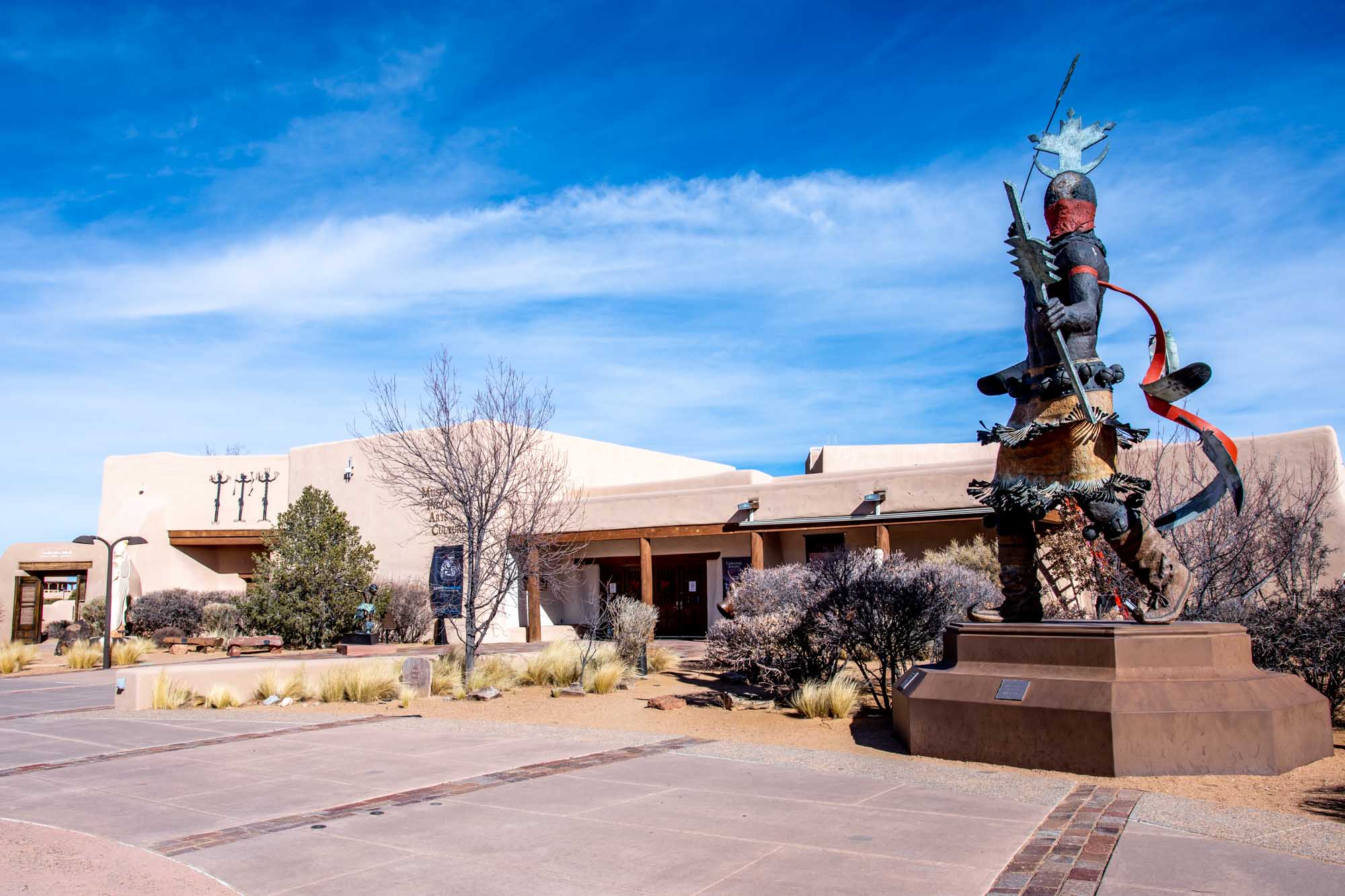 Statue of a Native American dancer outside a museum with an adobe facade in Santa Fe.