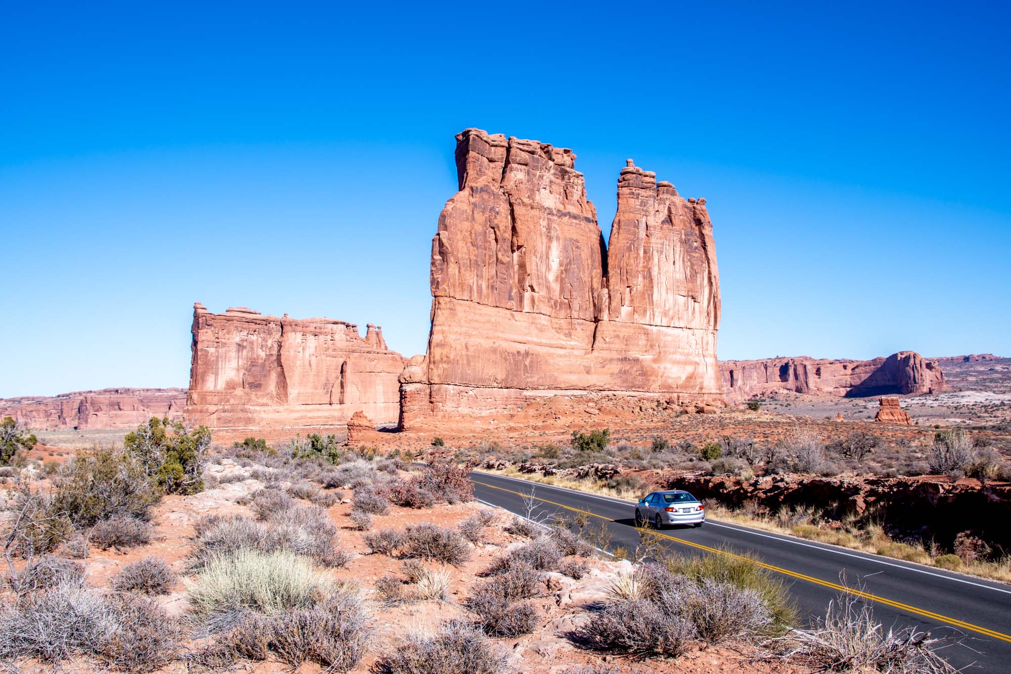 Car driving on road in front of Courthouse Towers rock formation