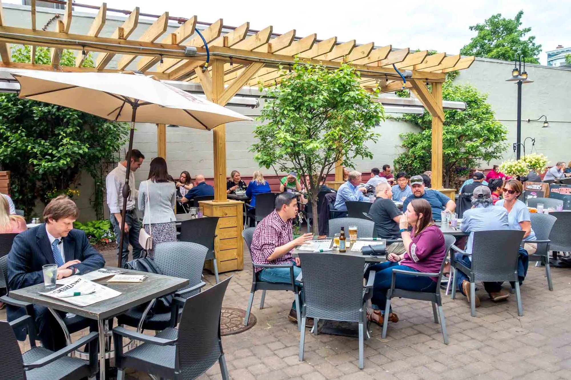 People sitting at outdoor tables under a pergola at a restaurant