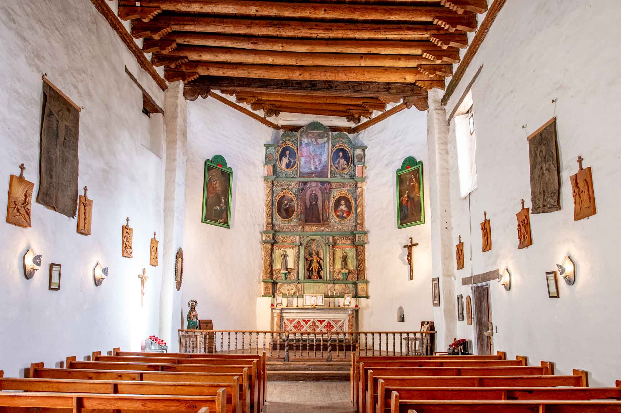 Chapel with pews, white walls, and a painted screen at the altar with multiple images of saints