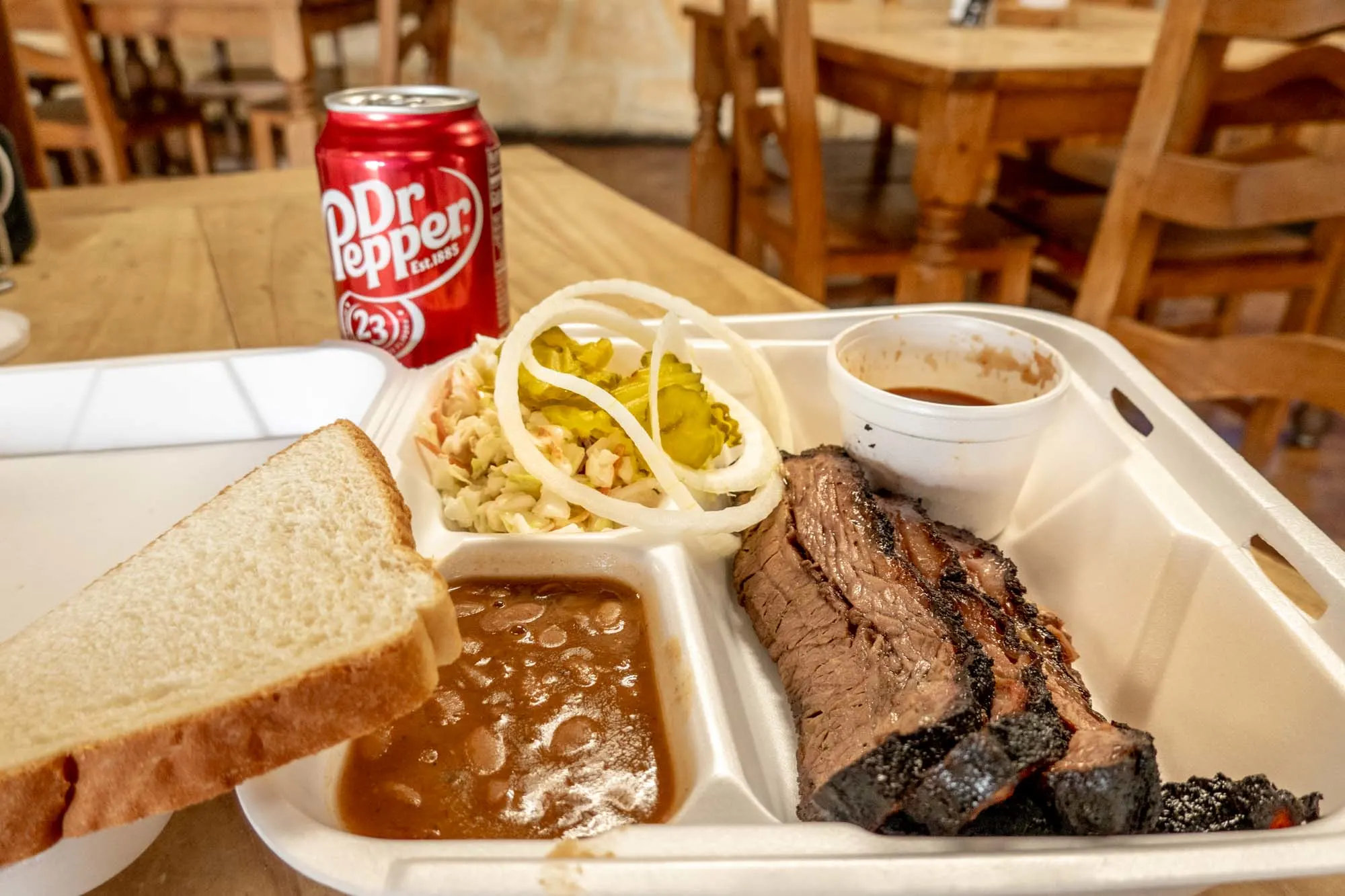 Container with beans, brisket, coleslaw, and bread beside a can of Dr. Pepper