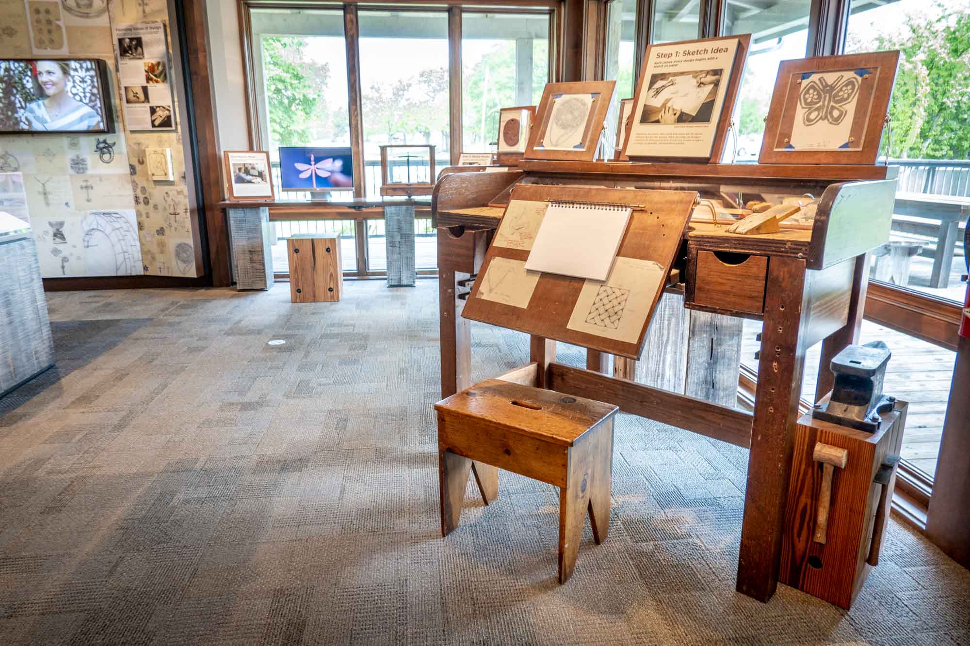 Museum display including a drafting table, sketch pads, and a video screen