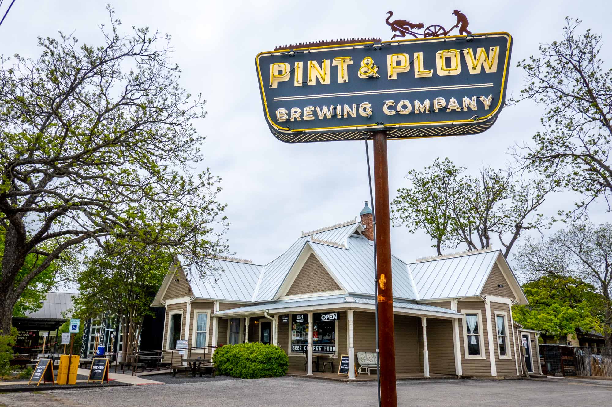Blue and yellow neon sign for Pint & Plow Brewing Company outside a one-story building