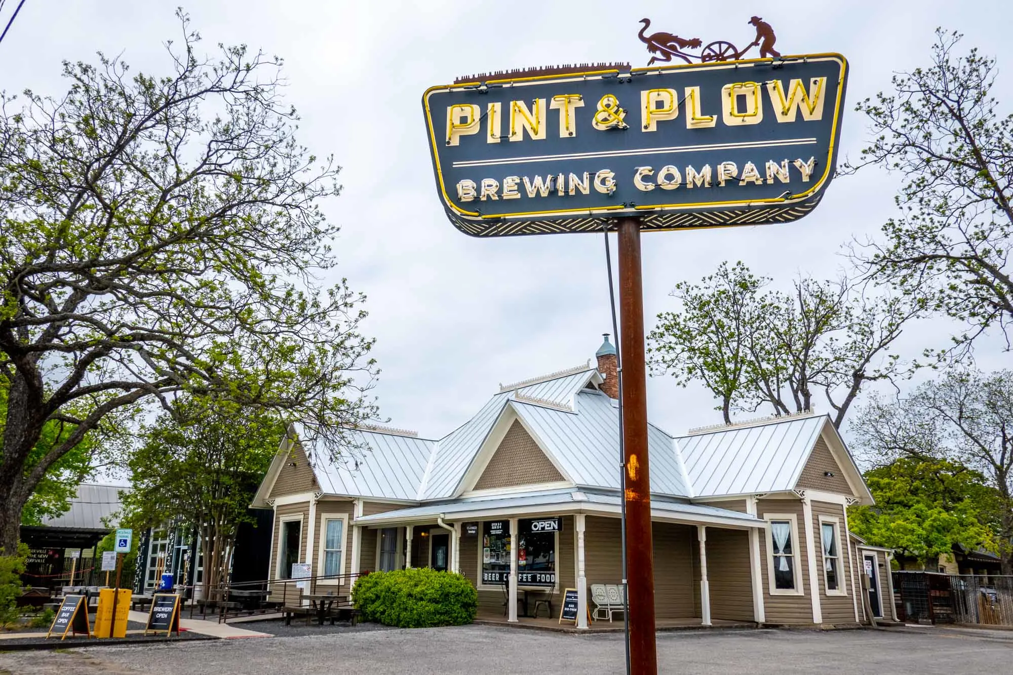 Blue and yellow neon sign for Pint & Plow Brewing Company outside a one-story building.