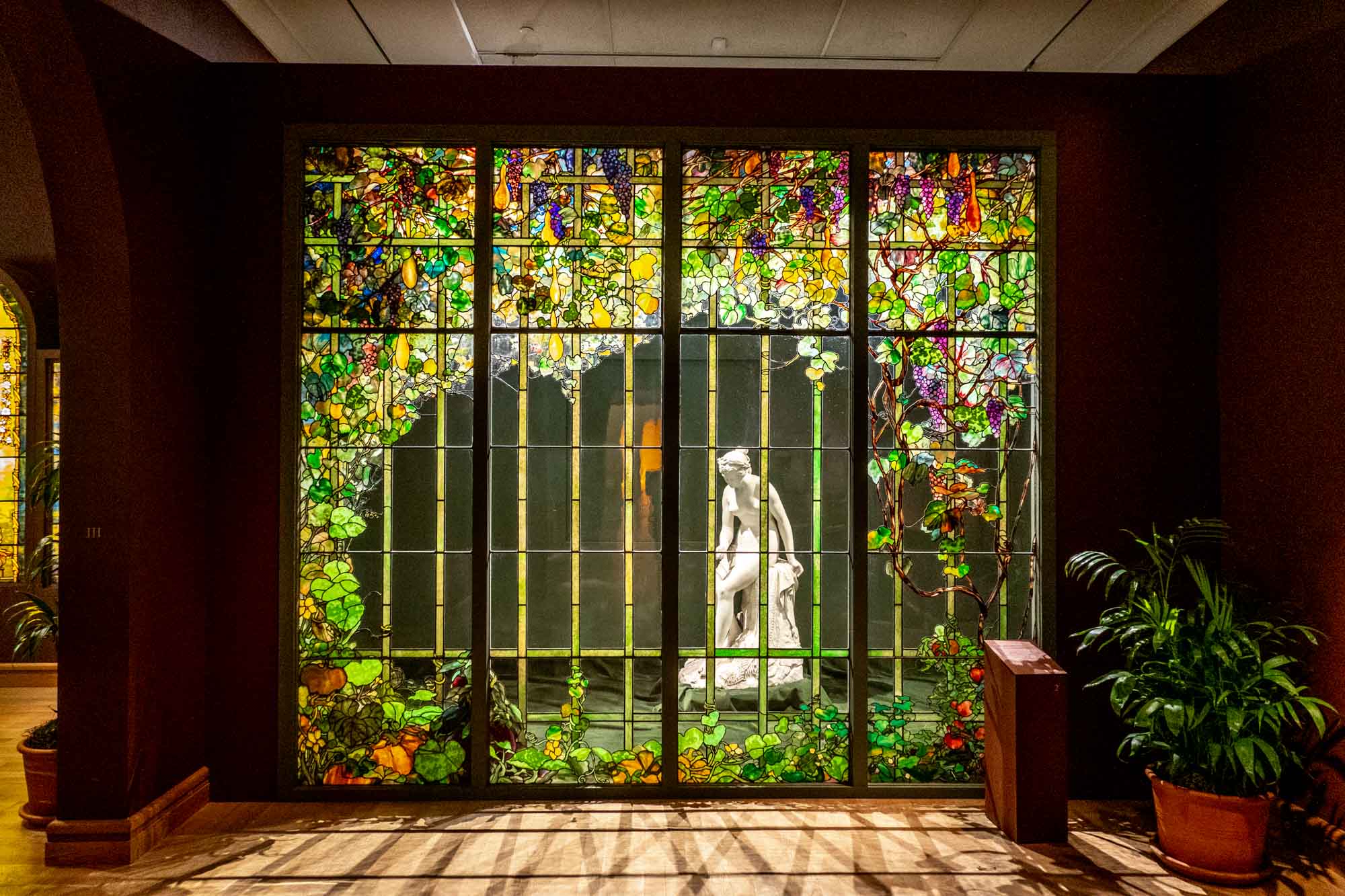 Panels of Tiffany leaded glass colored to look like flower vines in front of a marble statue of a woman