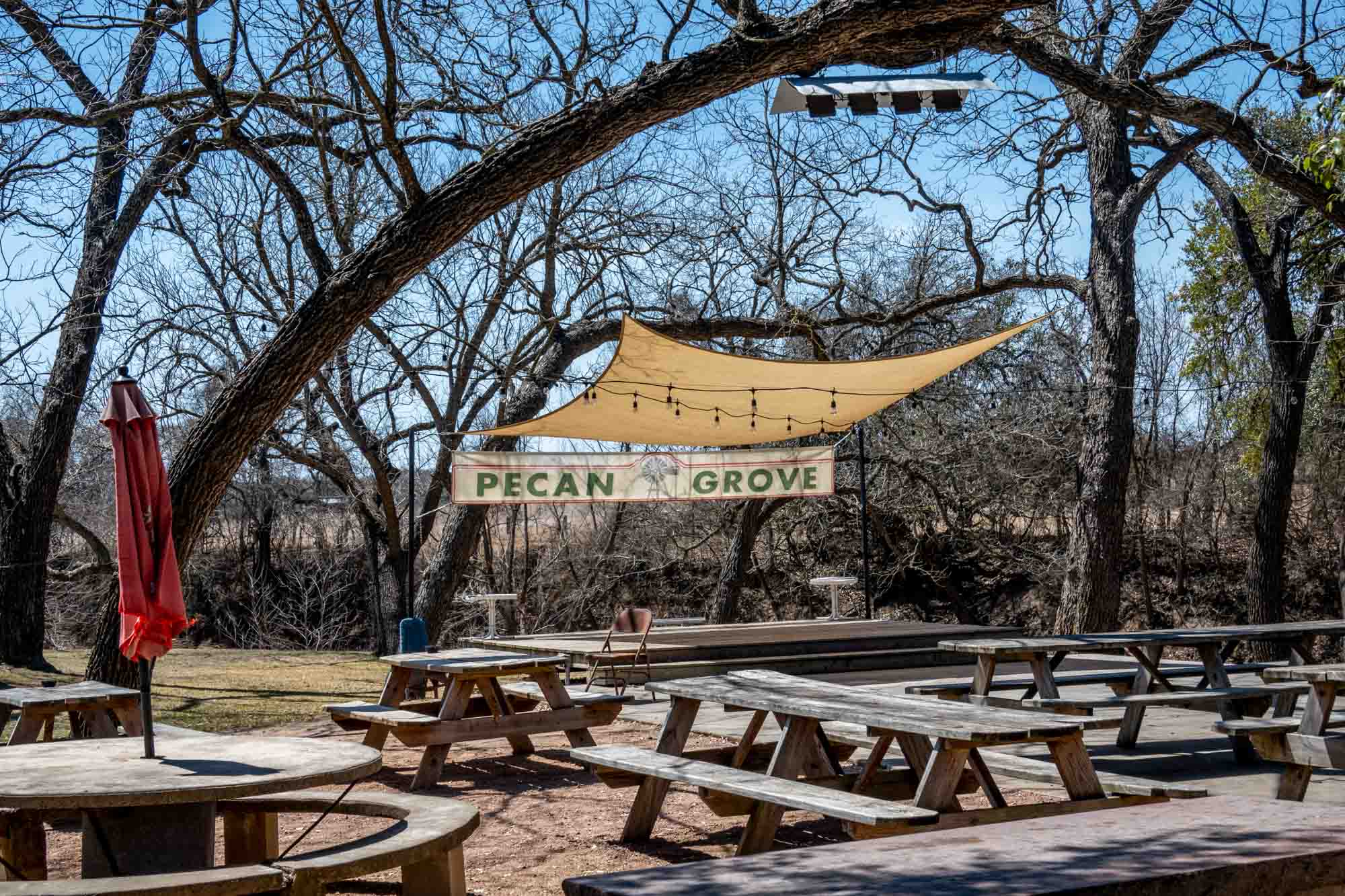 Picnic tables under trees with a wooden stage and sign for "Pecan Grove."