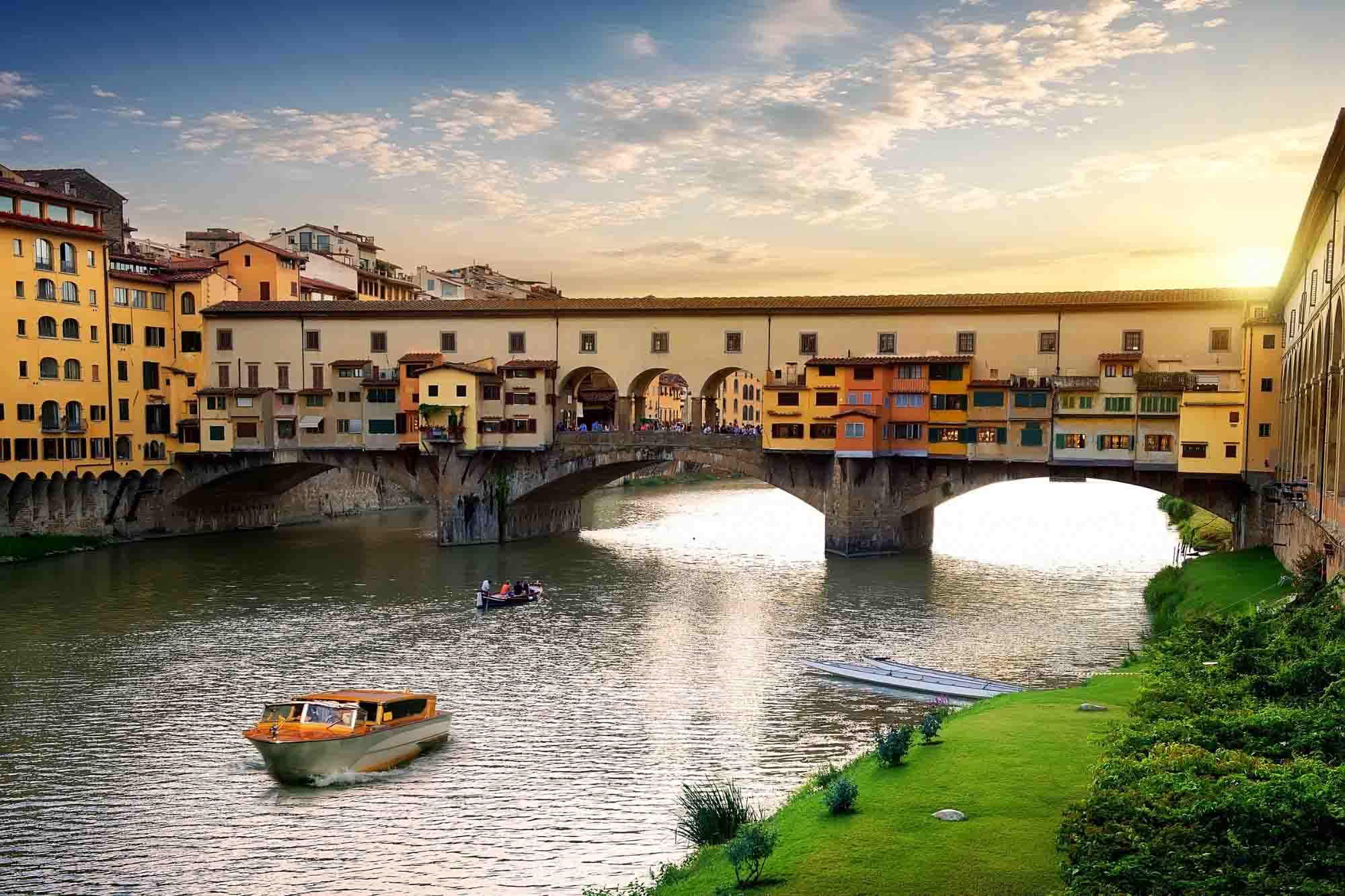 Boat in River Arno traveling under Ponte Vecchio bridge in Florence