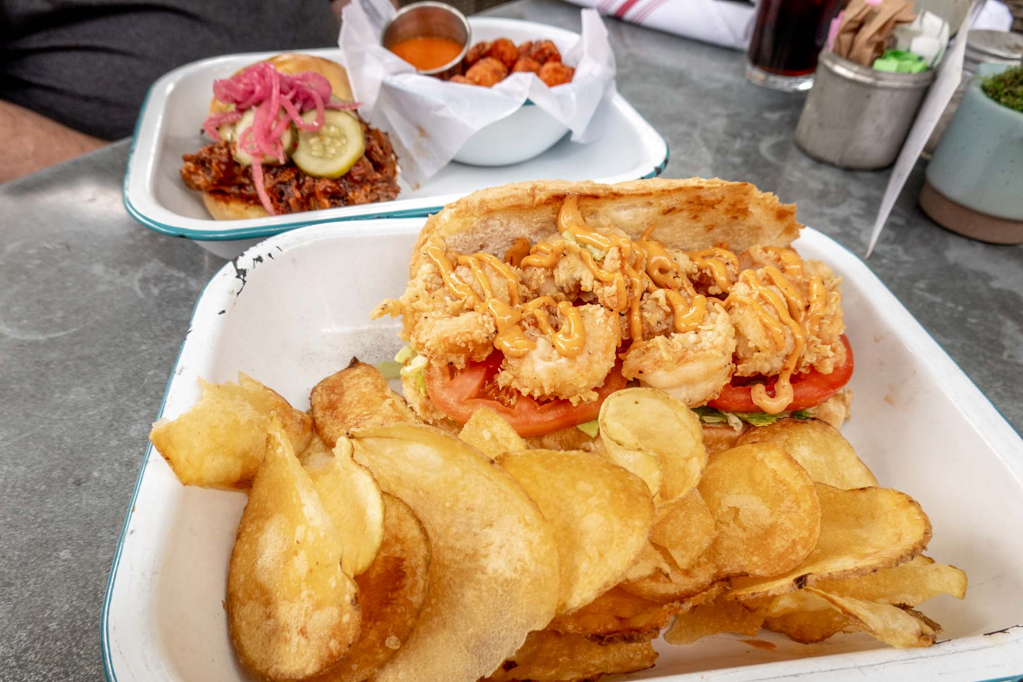 Shrimp poboy and potato chips on a plate beside a pulled pork sandwich