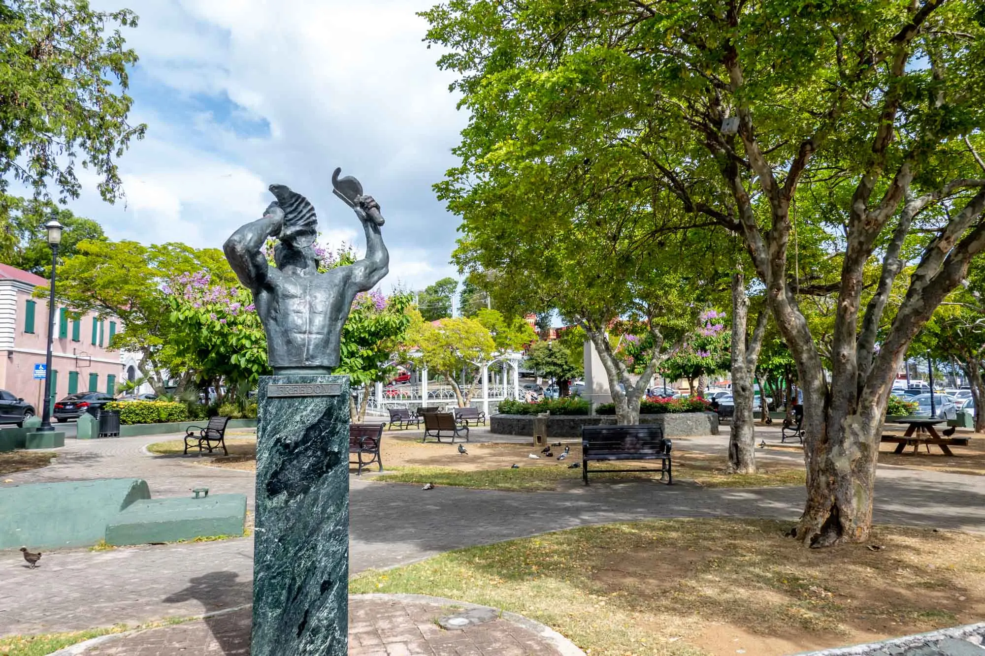 Statue of a man blowing a conch shell in a park with benches and trees