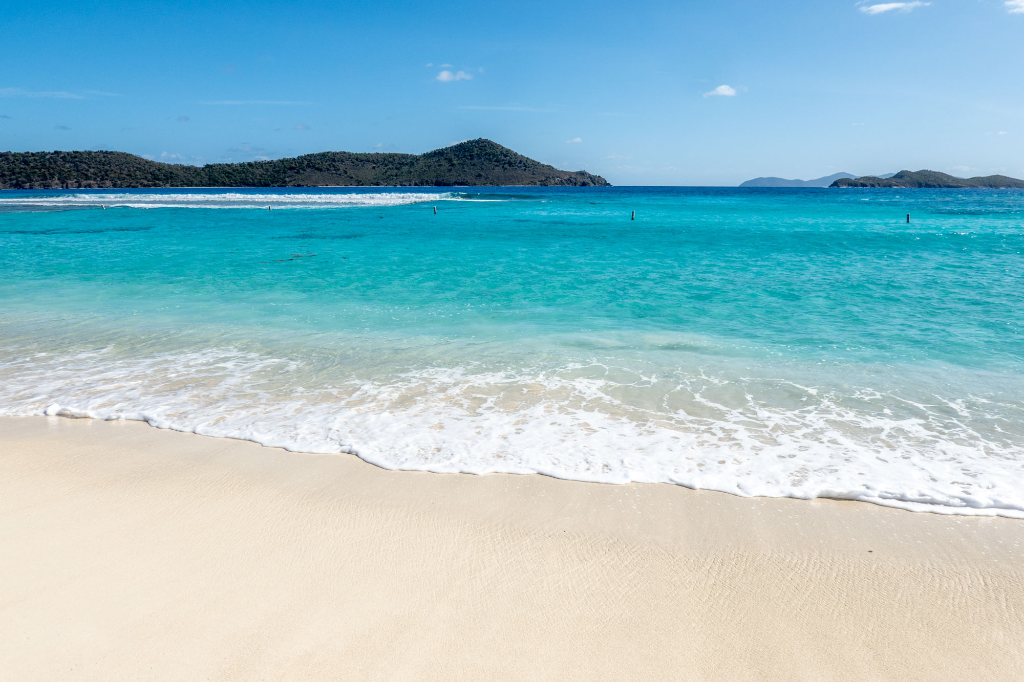 Blue ocean water and a white sand beach with hilly islands in the distance in St. Thomas