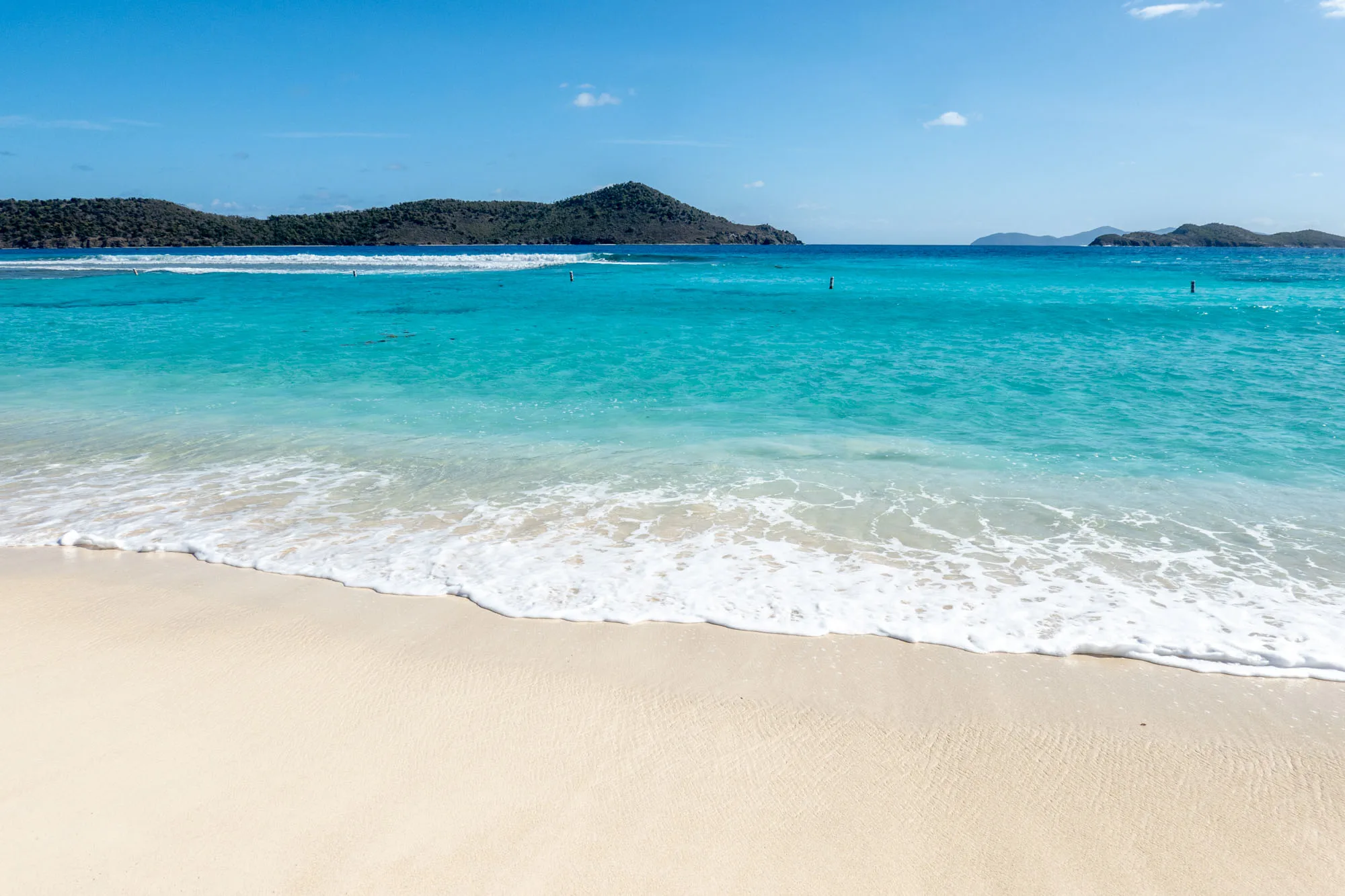 Blue ocean water and a white sand beach with hilly islands in the distance in St. Thomas