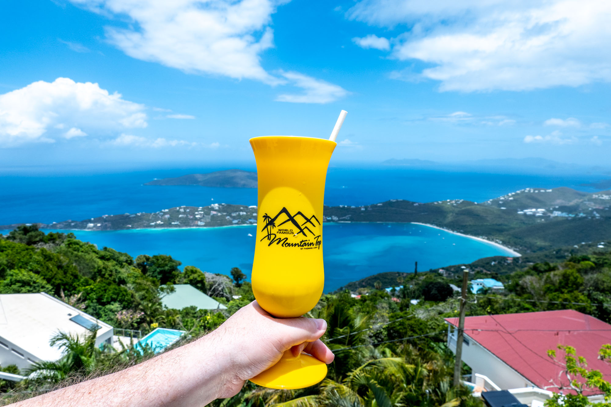 Hand holding a yellow cup labeled "Mountain Top" in front of a view of an island landscape.