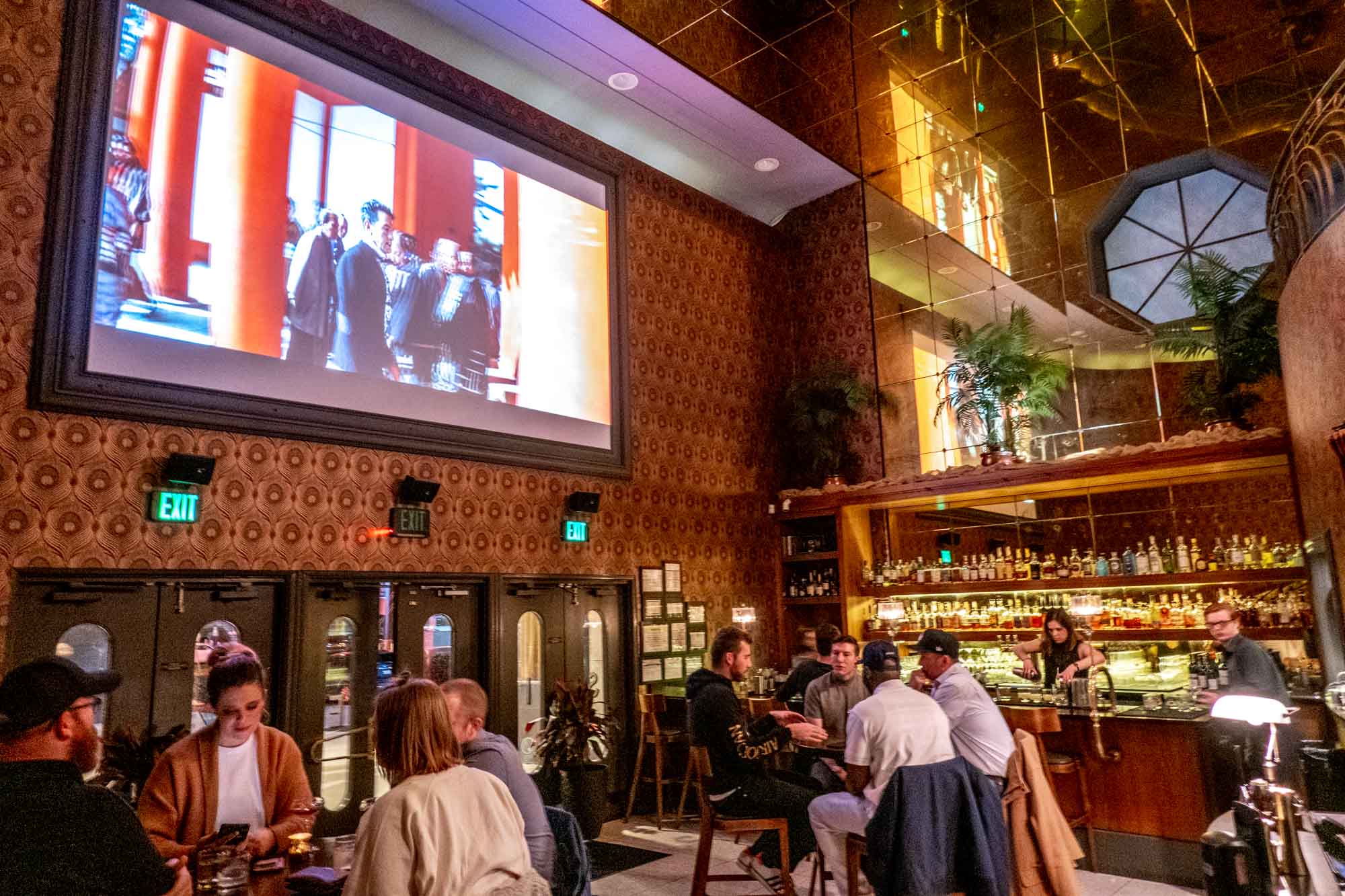 People seated at tables in a bar with a movie projected on the wall.