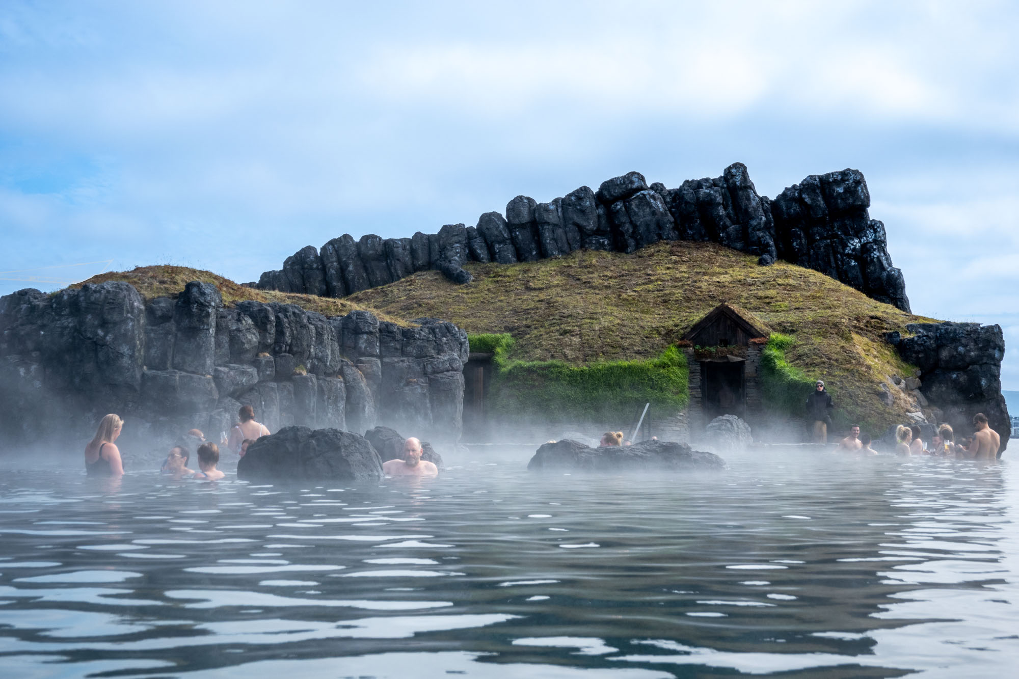 People in a hot spring lagoon in front of a small hill and rock formation