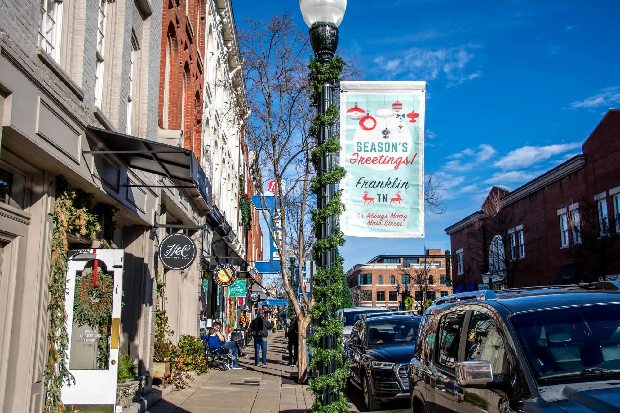 Garland-covered lamppost on a city street with a sign: Season's Greetings! Franklin, TN. It's always merry on Main Street!