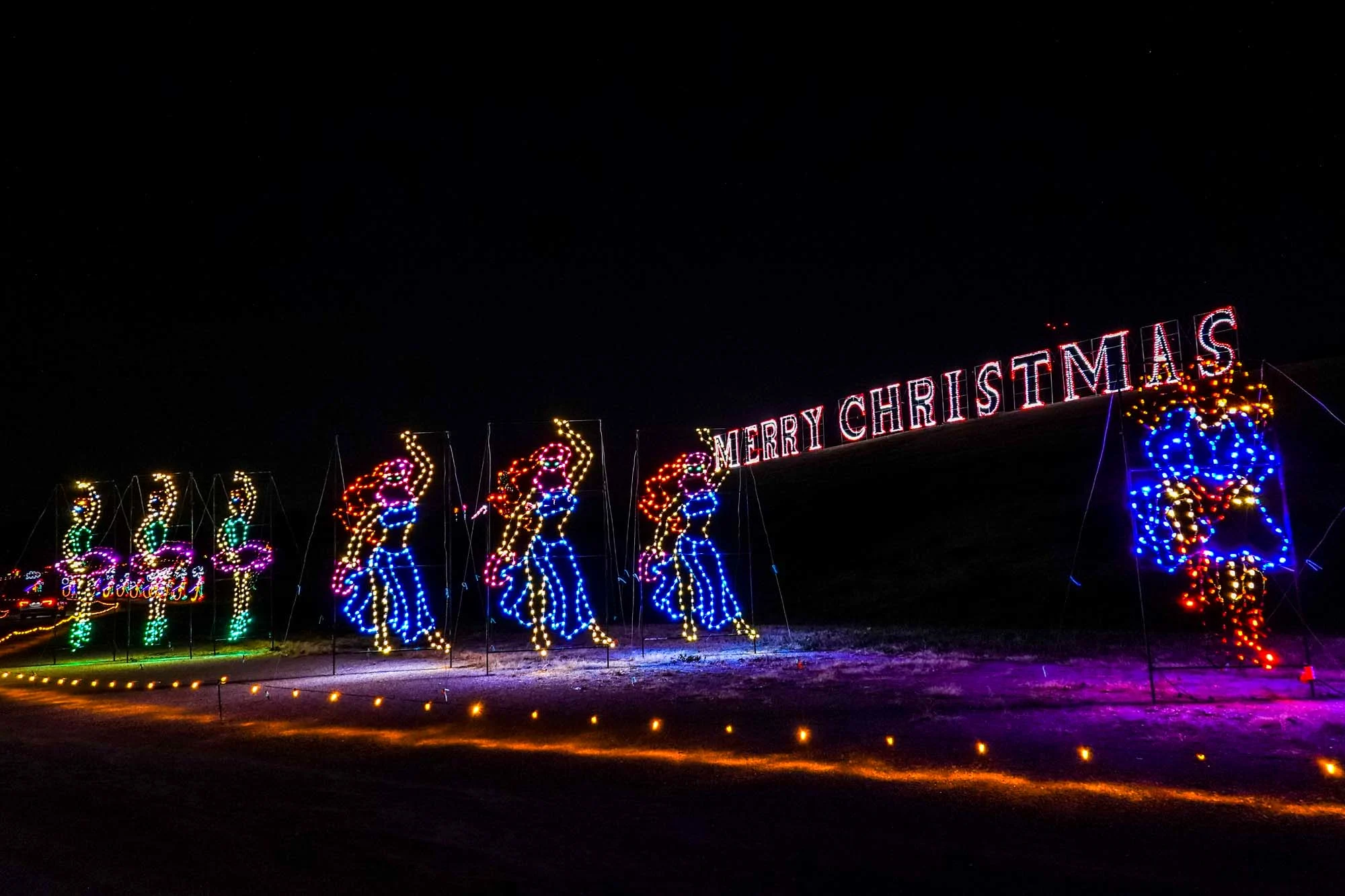 Christmas lights shaped like dancing women in front of a lit up "Merry Christmas" sign