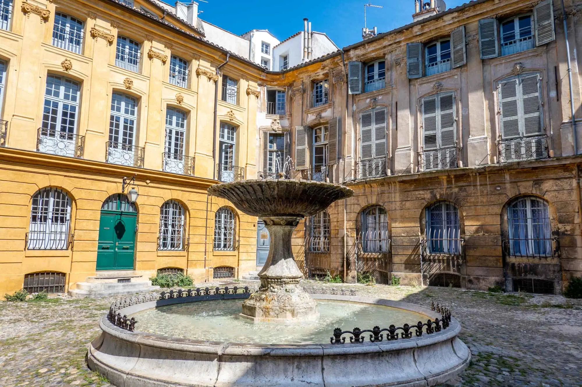 Fountain in a square surrounded by yellow buildings with wrought iron window decorations.