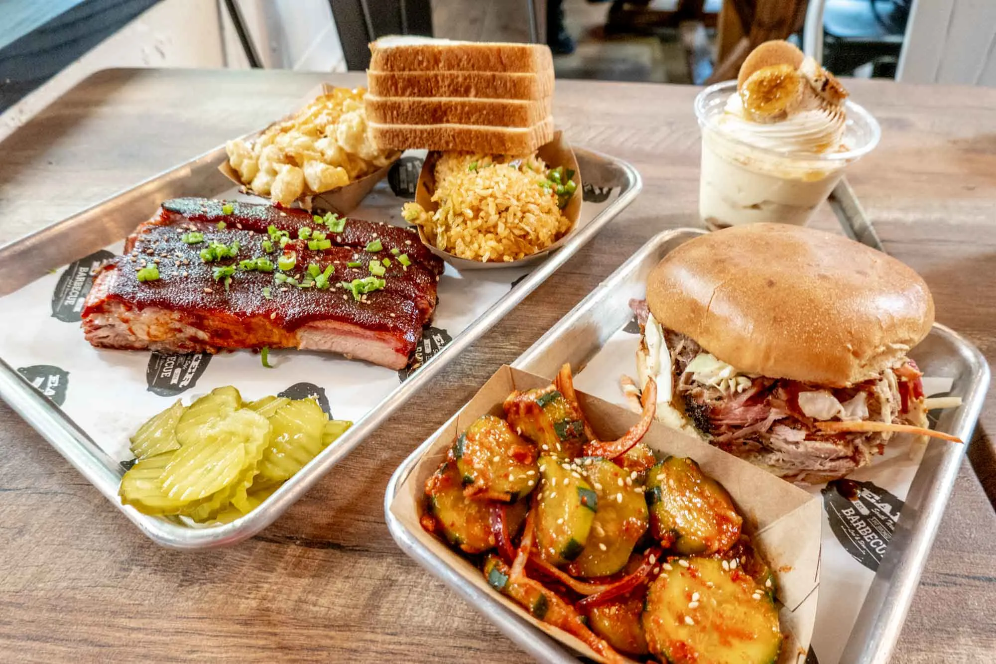 Ribs, pulled pork sandwich, pickles, and other food on table.