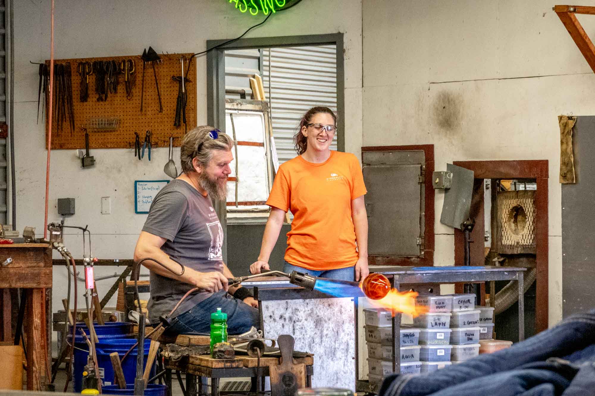 People in a glassblowing workshop using a blowtorch on a piece of molten glass